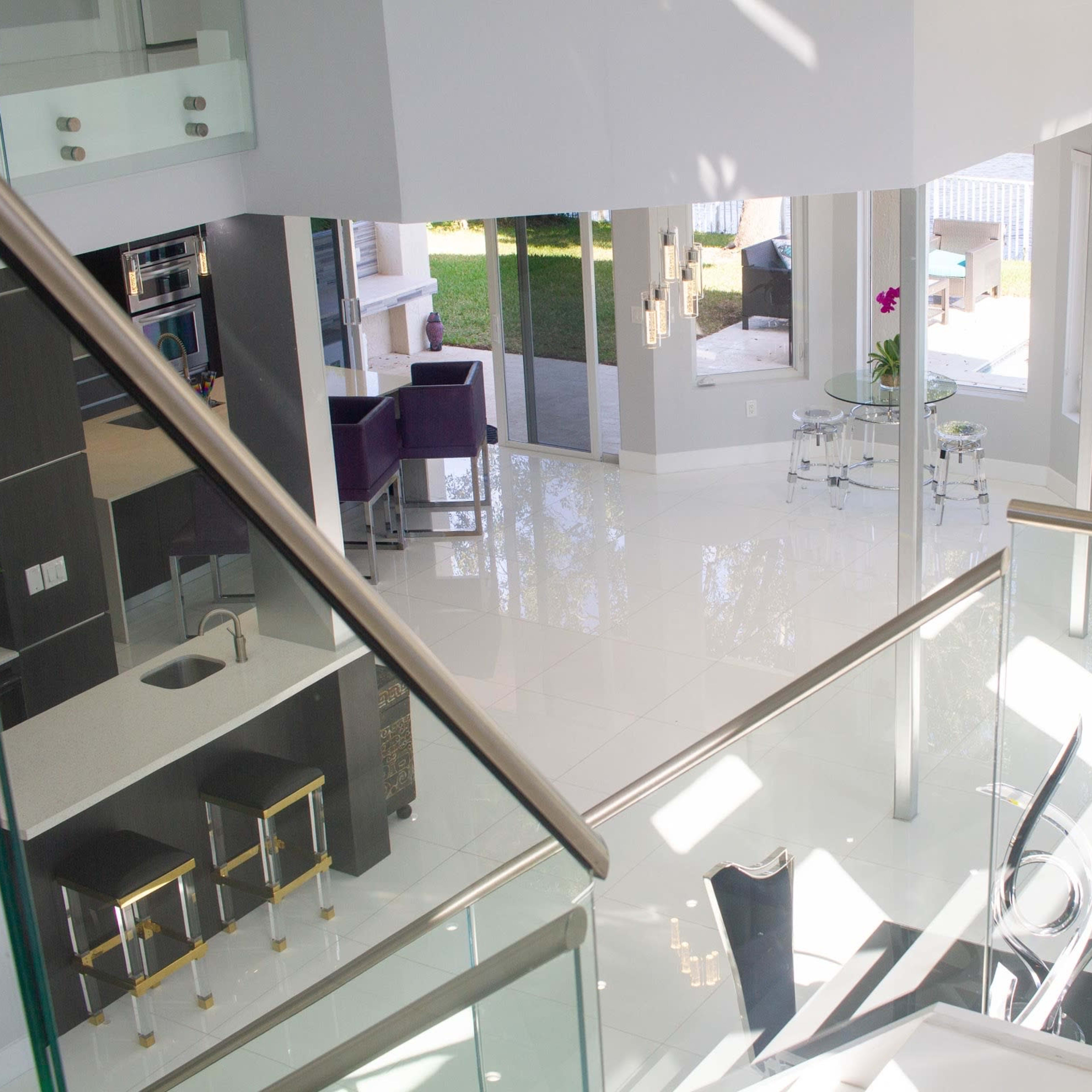 A modern, open-concept living space with a glass railing overlooking a bright, luminous area featuring sleek furniture and large windows.