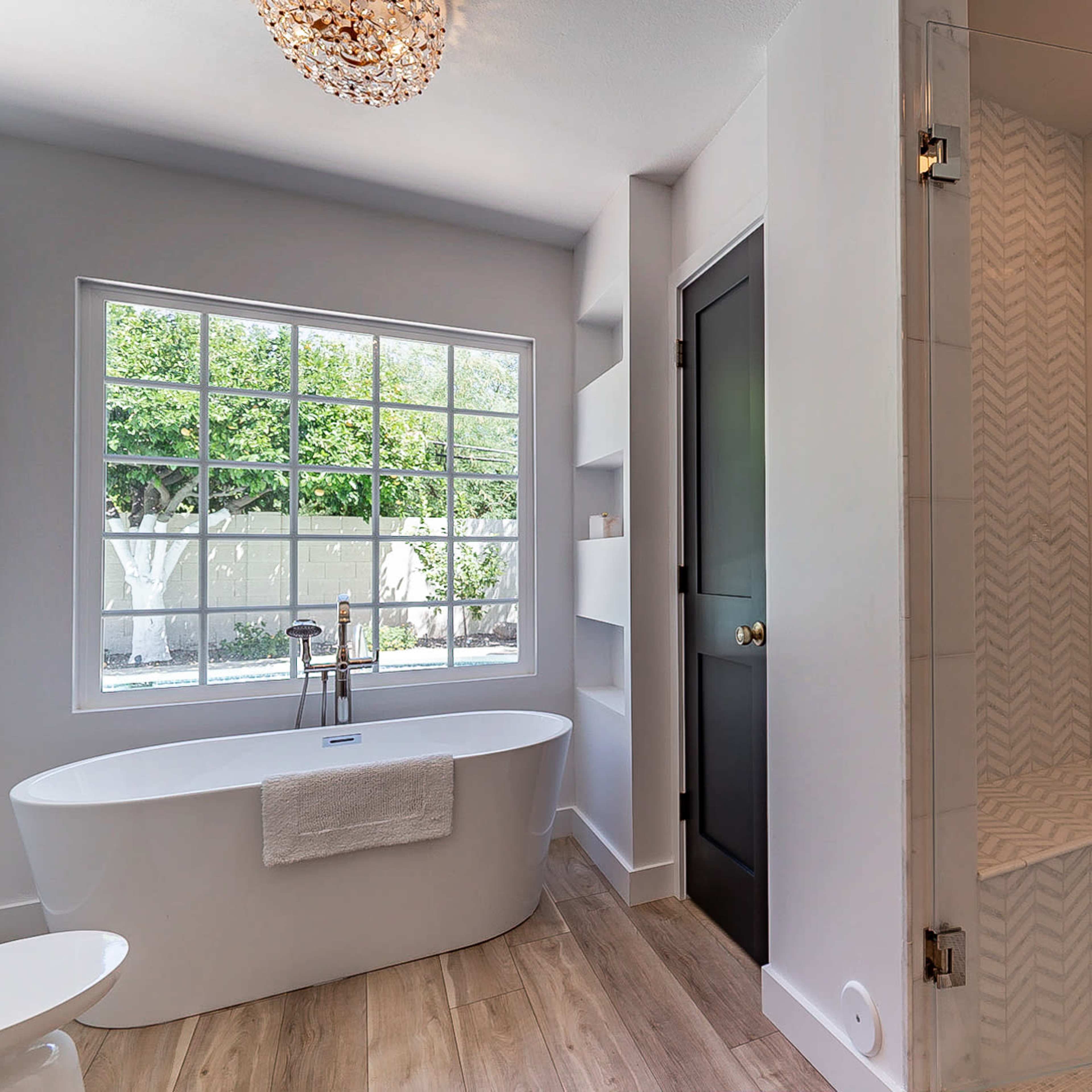 A modern bathroom featuring a freestanding bathtub beside a glass shower enclosure, with a large window providing natural light.