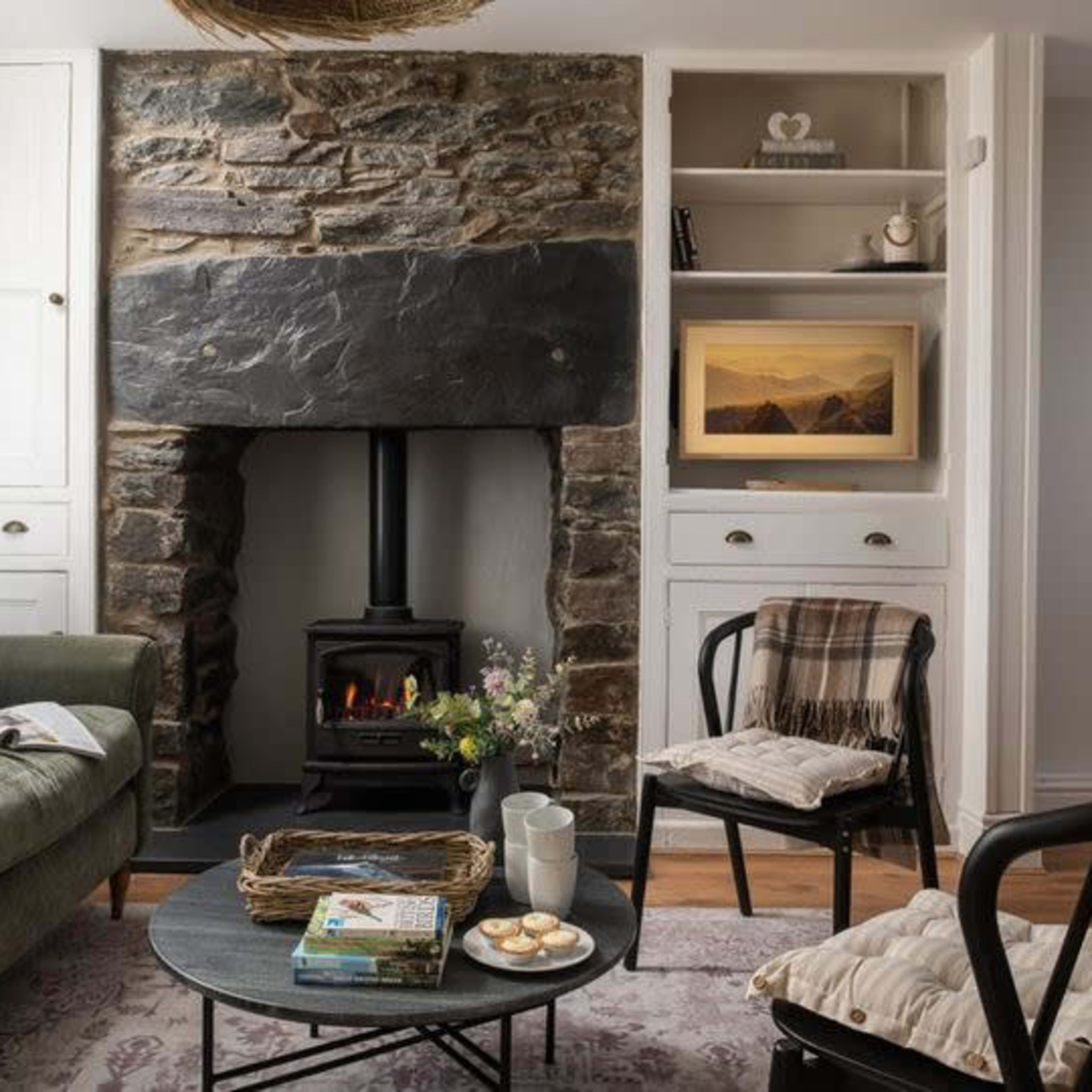 A cozy living room features a stone fireplace, a green sofa, and a round coffee table adorned with cookies and a magazine.