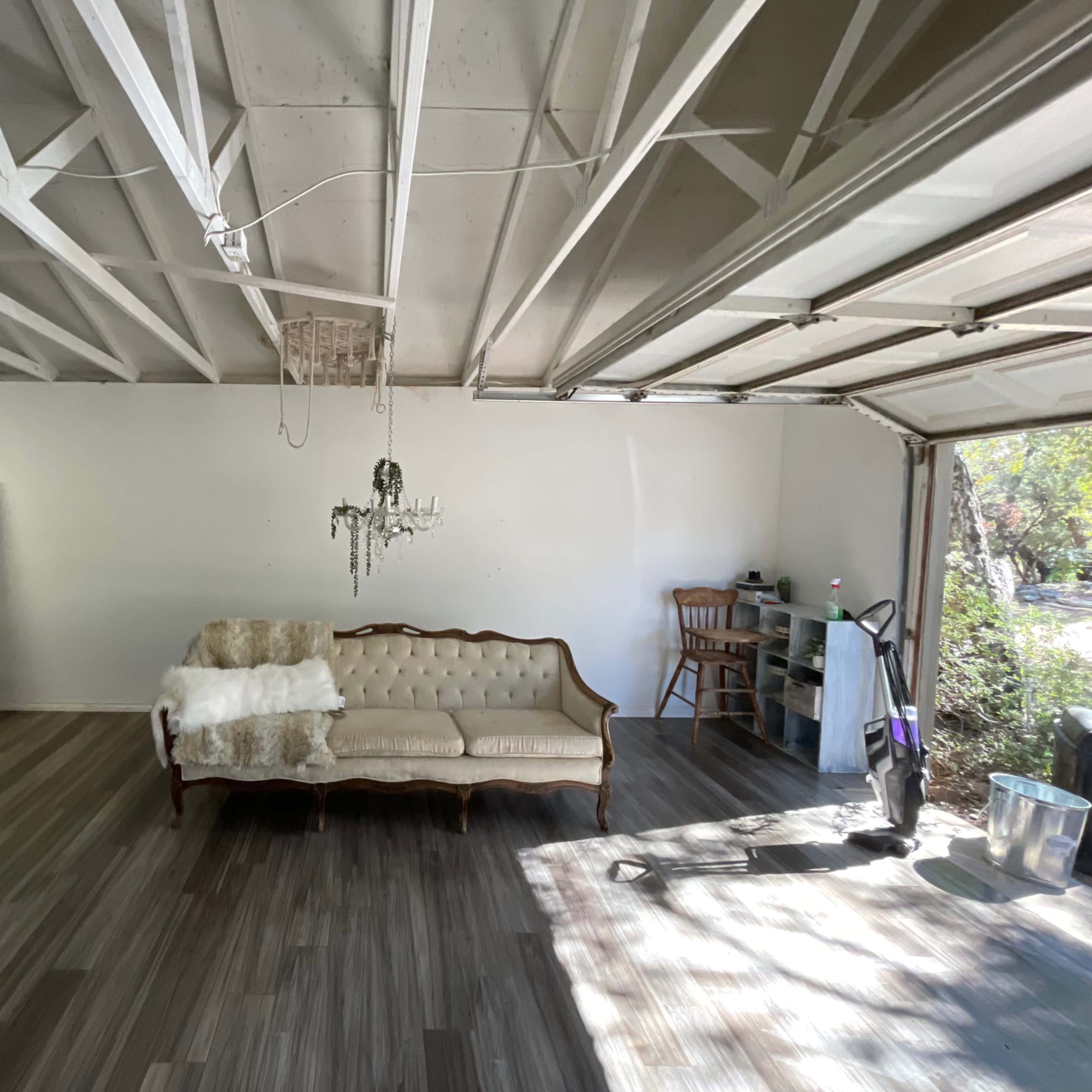 A bare garage features a couch, a toilet, a chandelier, and various pieces of furniture against white walls.