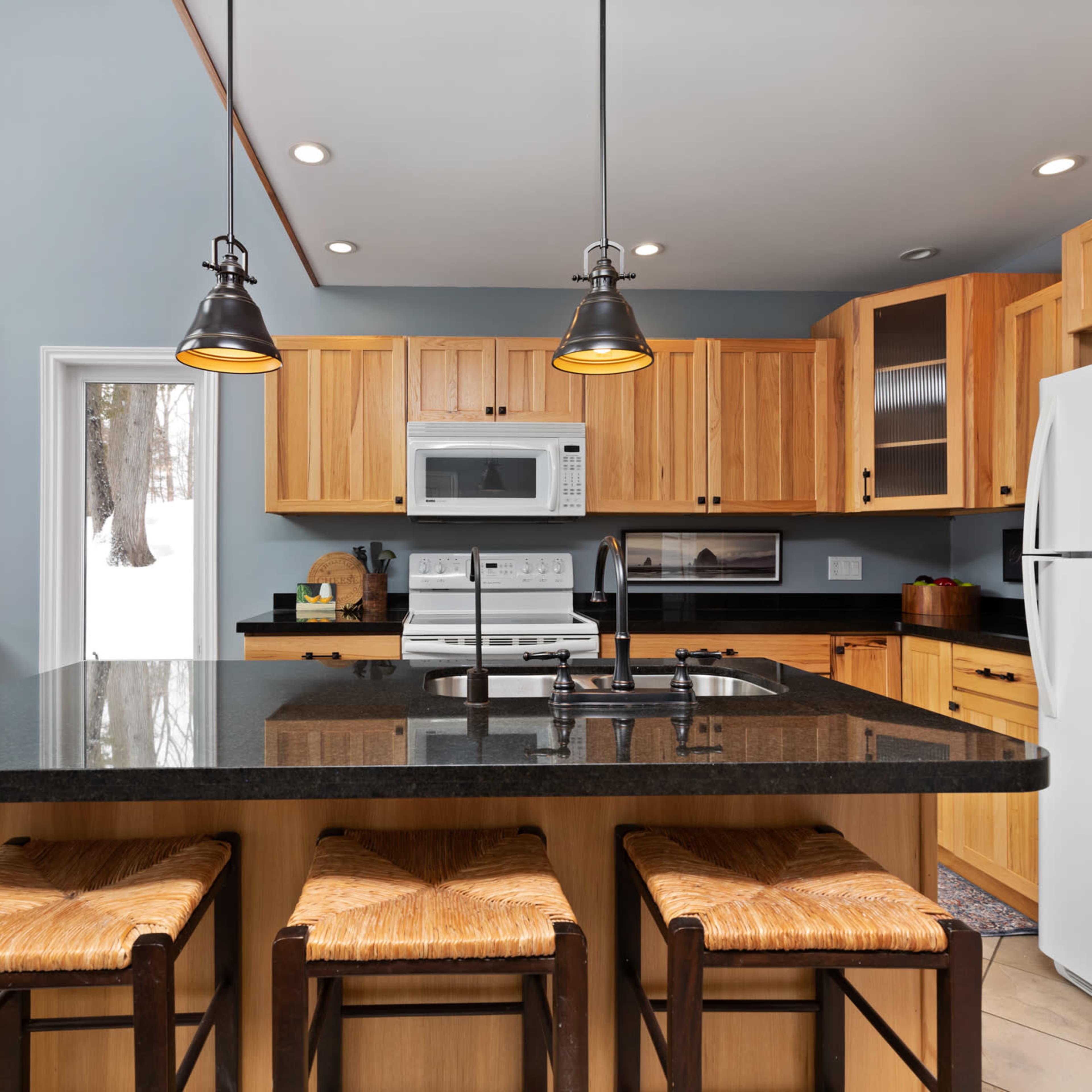 A modern kitchen features wooden cabinets, a black granite island with seating, and stainless steel appliances.