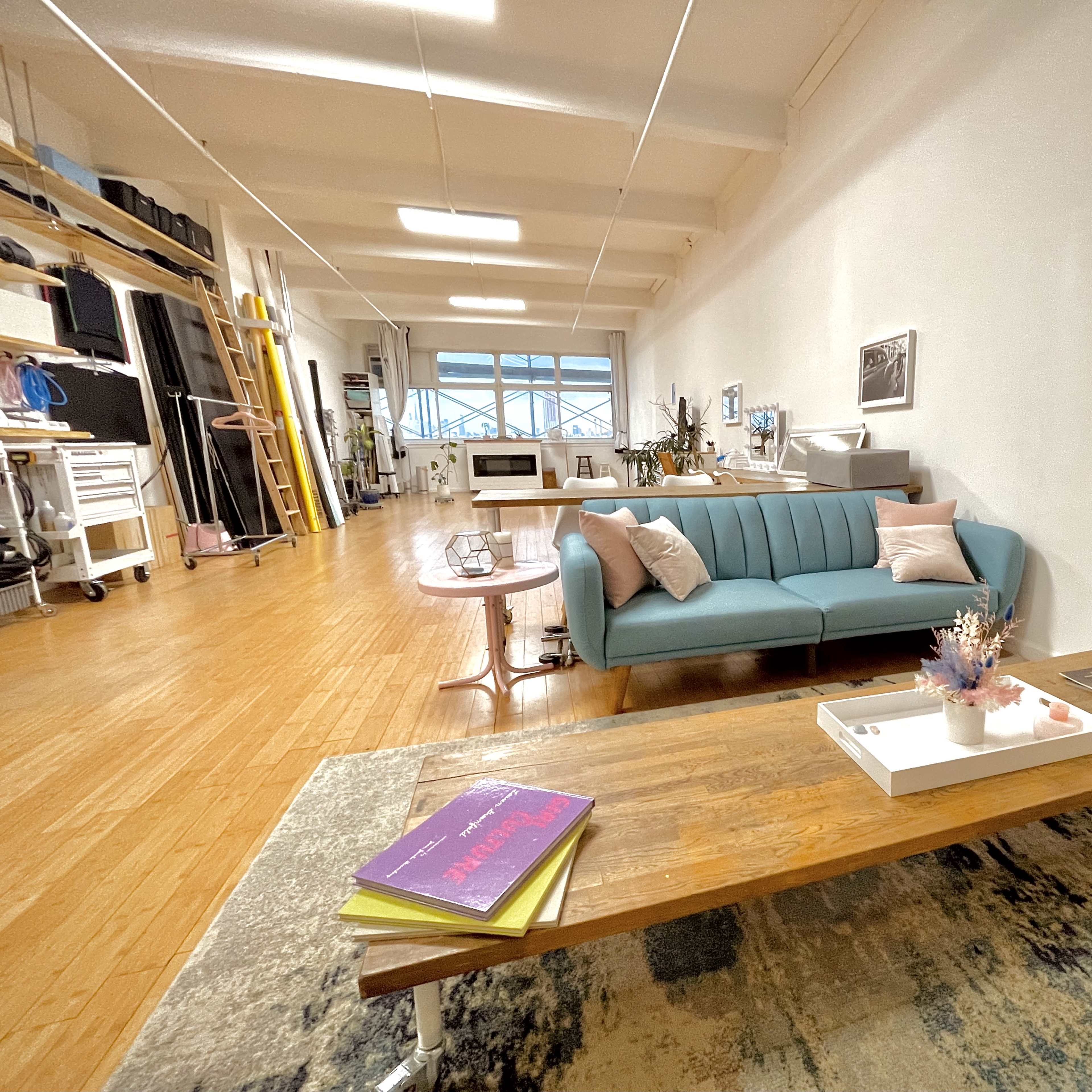 A spacious room featuring a light blue couch, a wooden coffee table with books, and a variety of furniture and decor items in a bright, well-lit environment.
