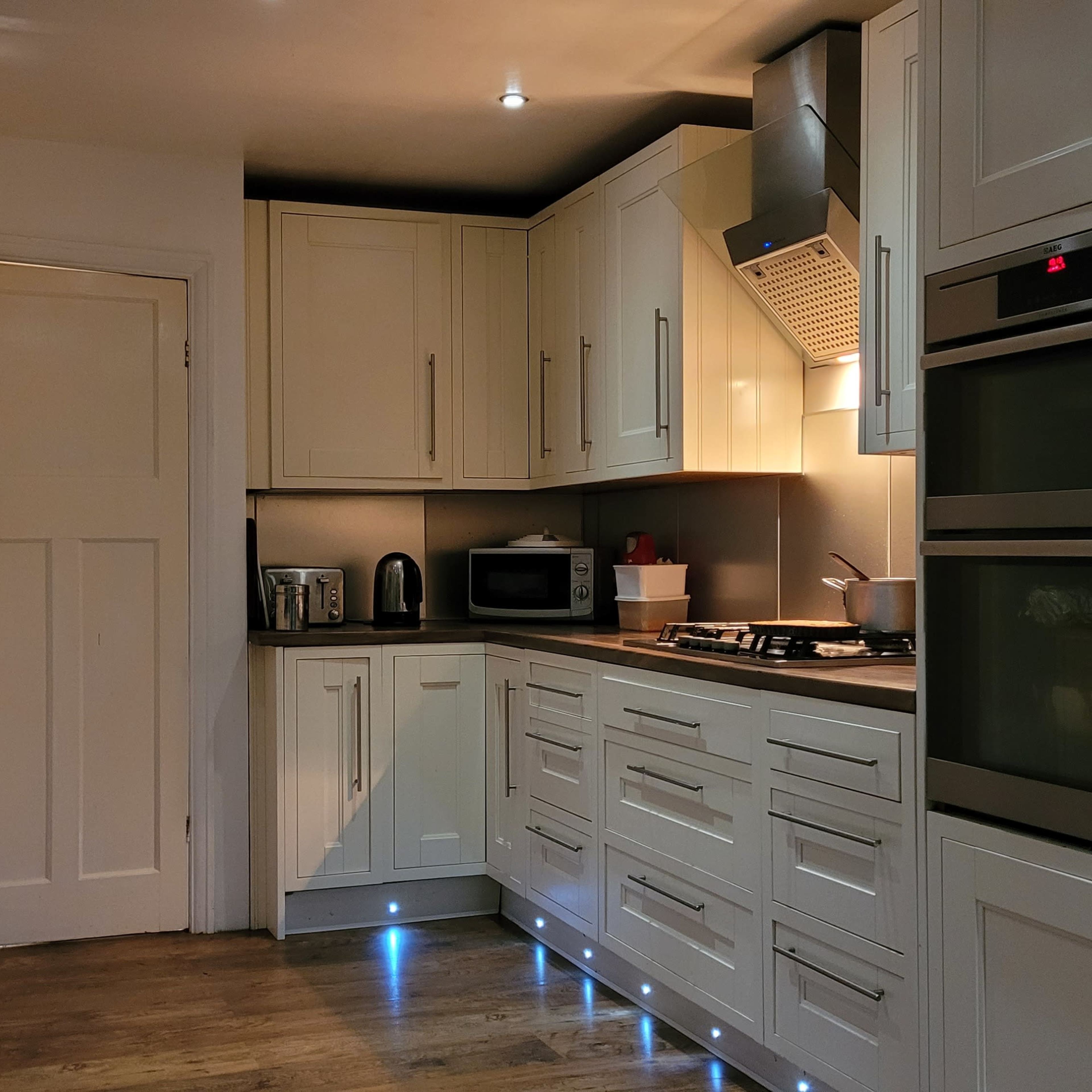A modern kitchen featuring white cabinets, stainless steel appliances, and a wooden countertop with under-cabinet lighting.