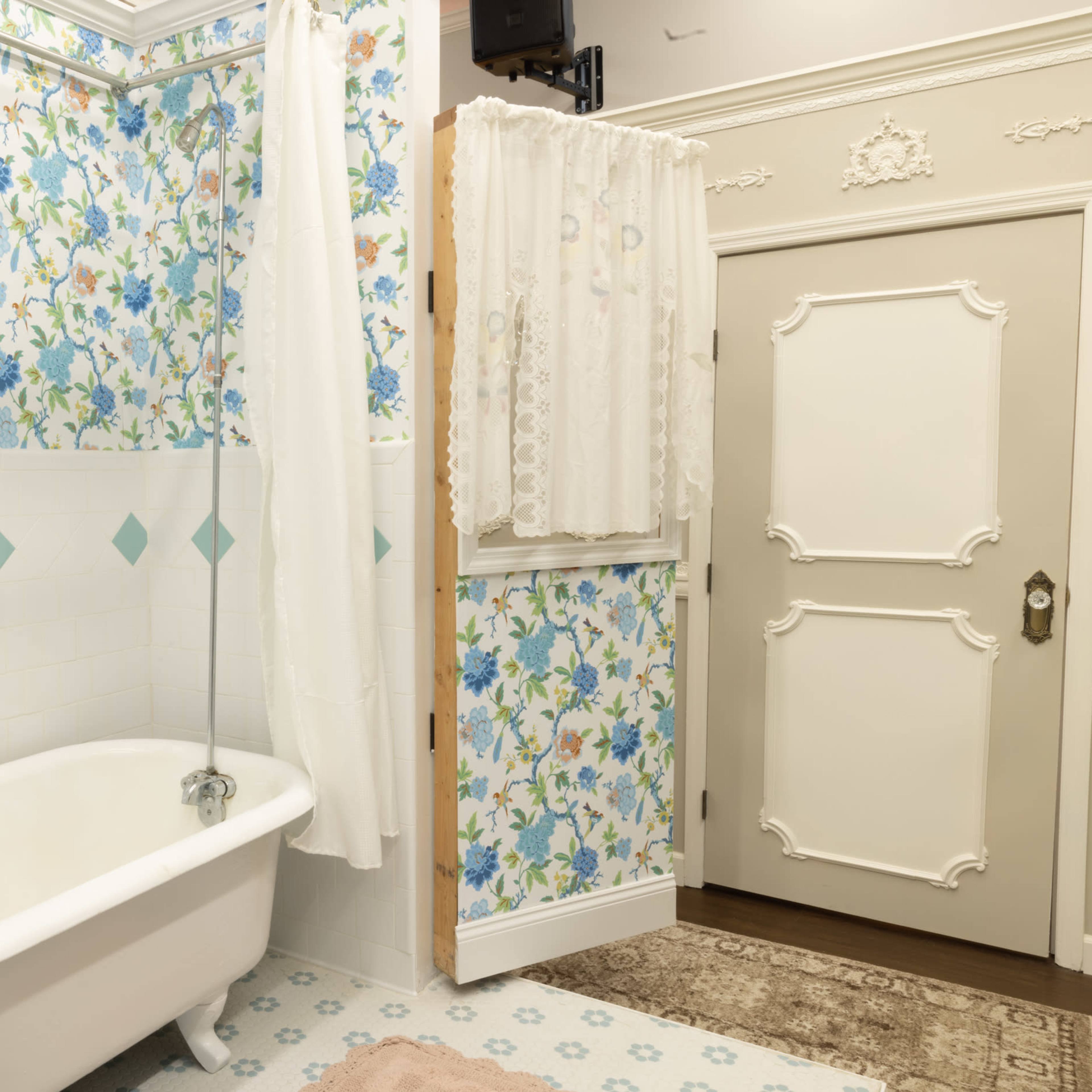 A bathroom featuring a clawfoot bathtub, floral wallpaper, and a door with decorative trim.