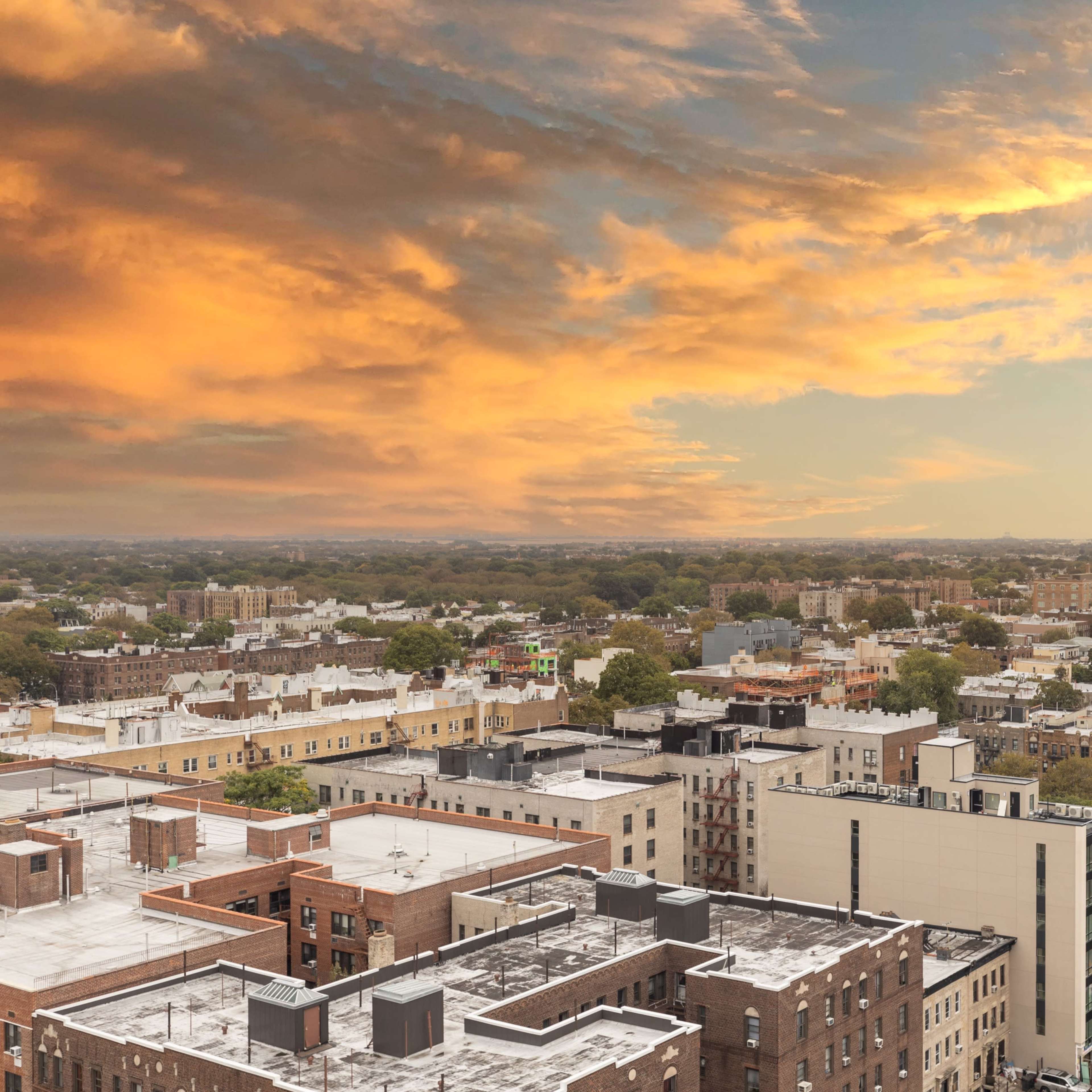 An aerial view of a city skyline during sunset, featuring a mix of residential and commercial buildings with a colorful sky above.