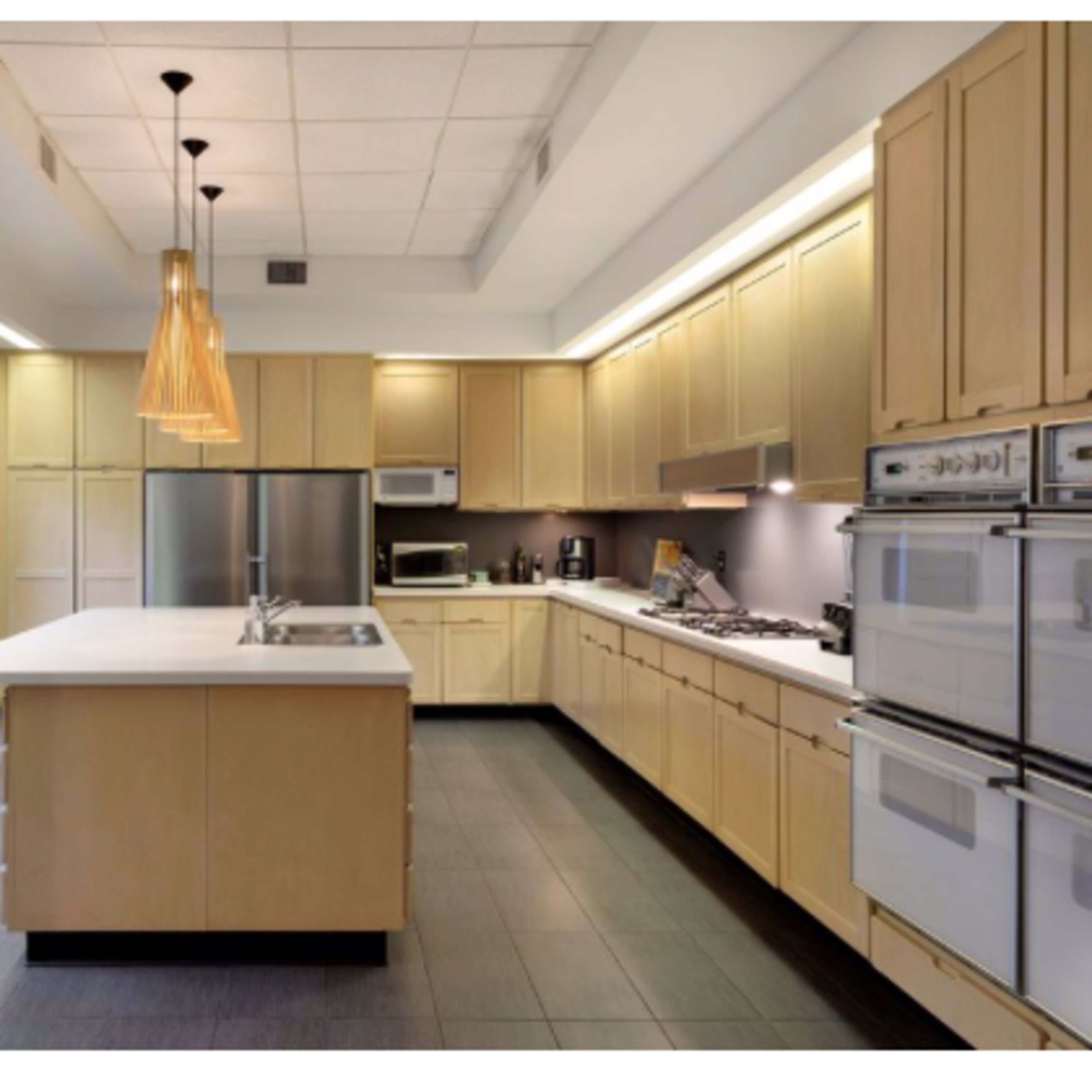 A modern kitchen with light wood cabinets, stainless steel appliances, and an island with a sink in the center.