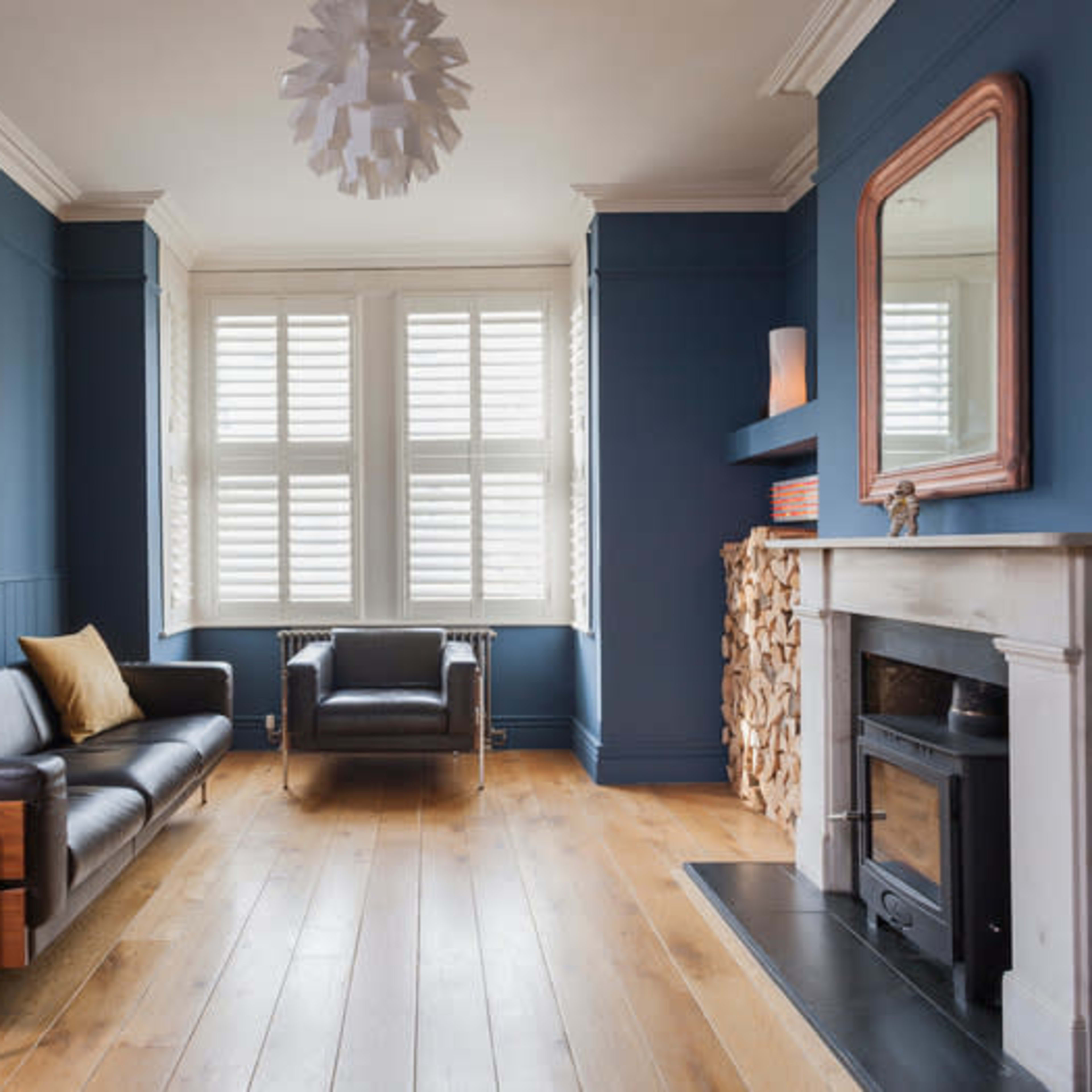 A modern living room with dark blue walls, a black leather sofa, a pair of armchairs, and a fireplace with a decorative log feature.