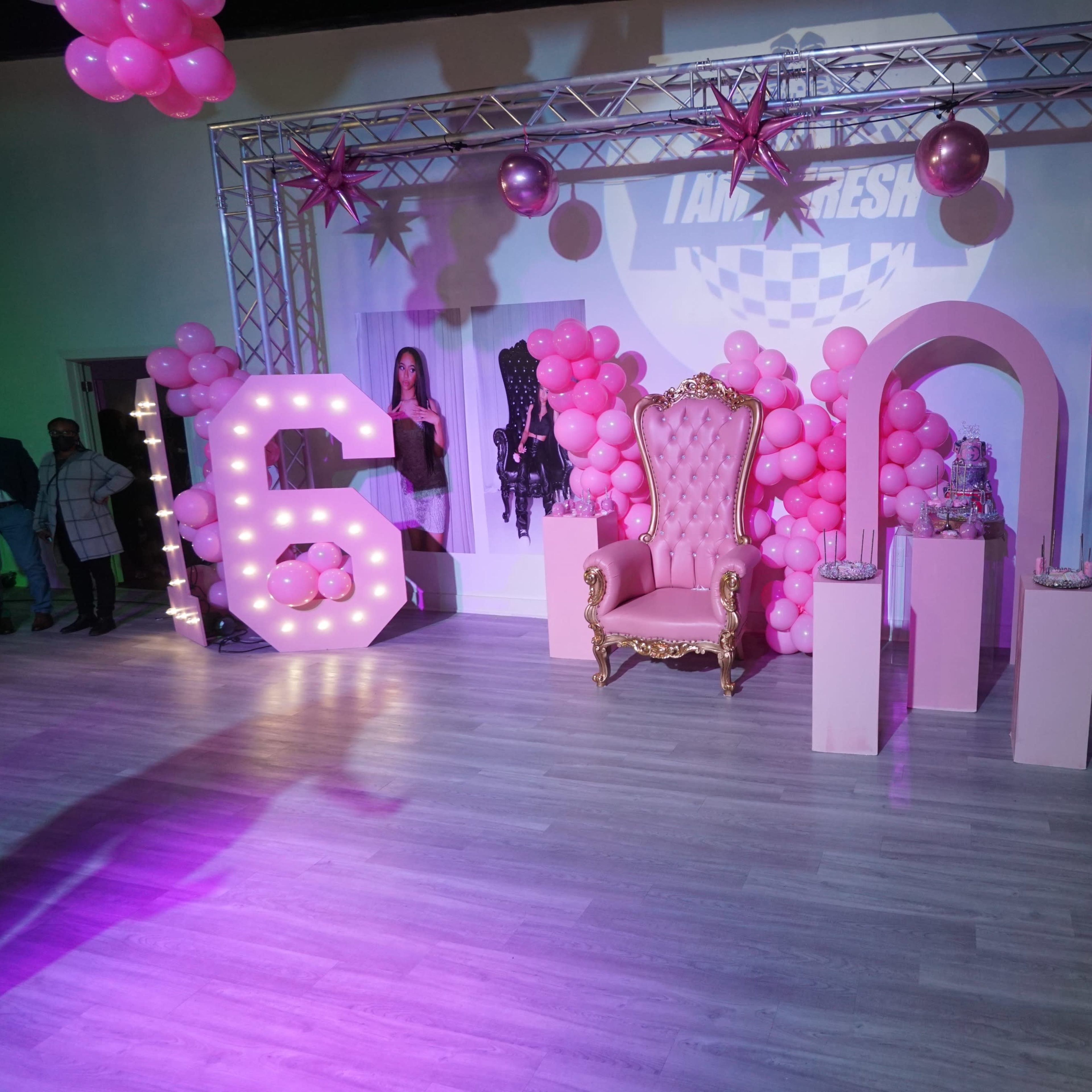 The scene features a pink-themed party setup with a large illuminated "6," a decorative throne, and balloon arrangements.