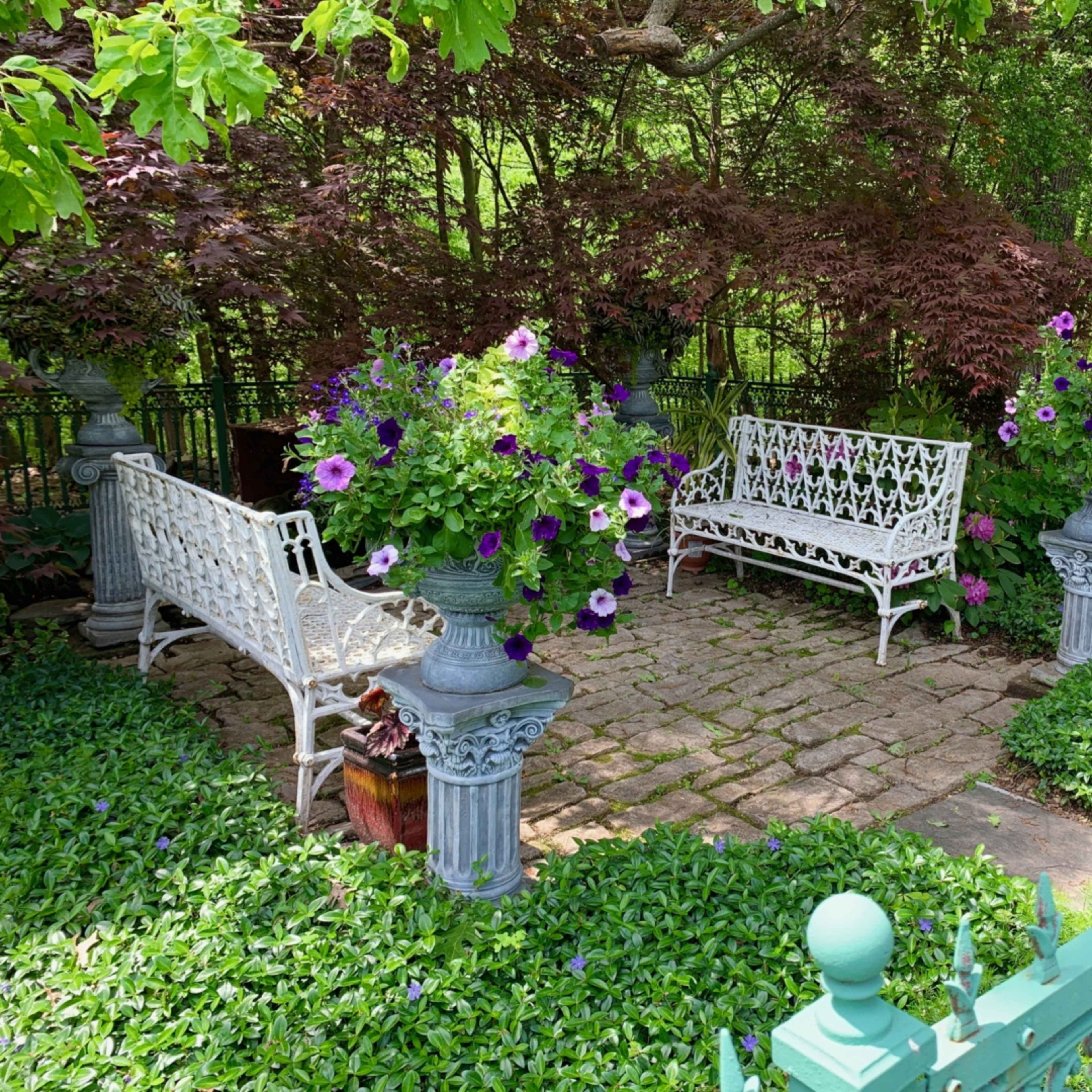 A serene garden area with two white benches surrounded by colorful flower pots and lush greenery.