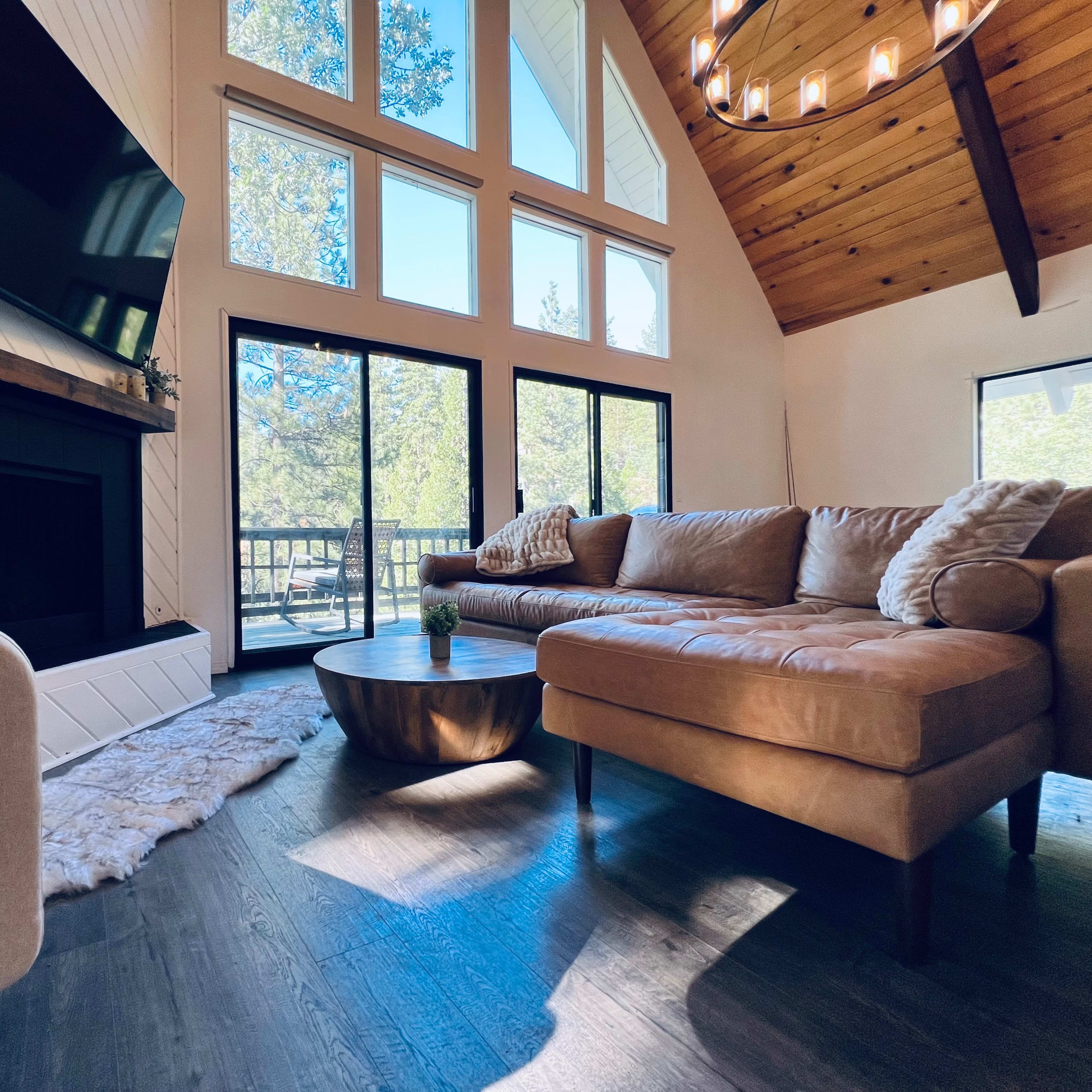 A cozy living room with a large window, a sectional sofa, a circular coffee table, and a fireplace, all illuminated by natural light.