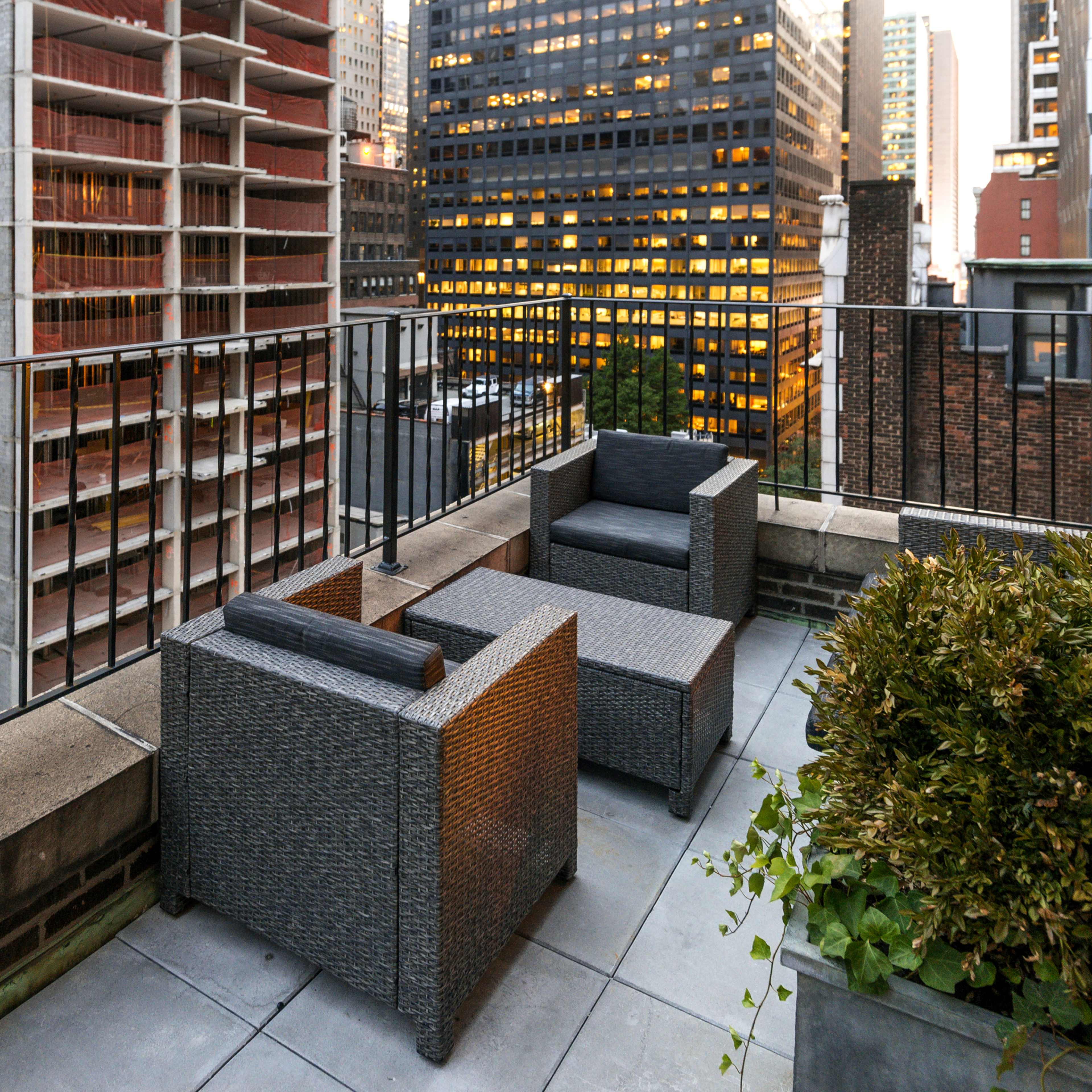 A rooftop terrace with two wicker chairs overlooking a city skyline during twilight.