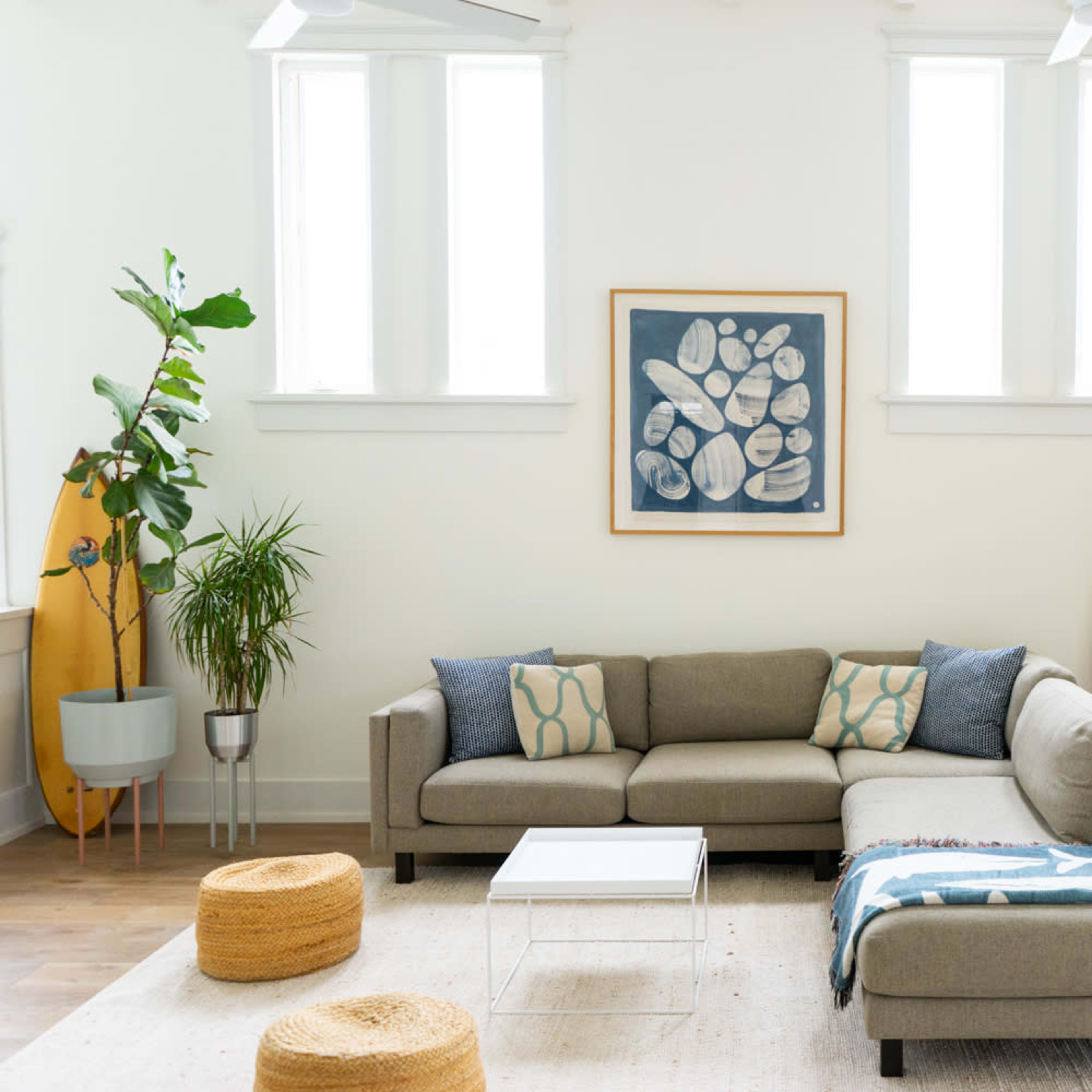 A modern living room featuring a sectional sofa, two round stools, a fireplace, and surfboards leaning against the wall.