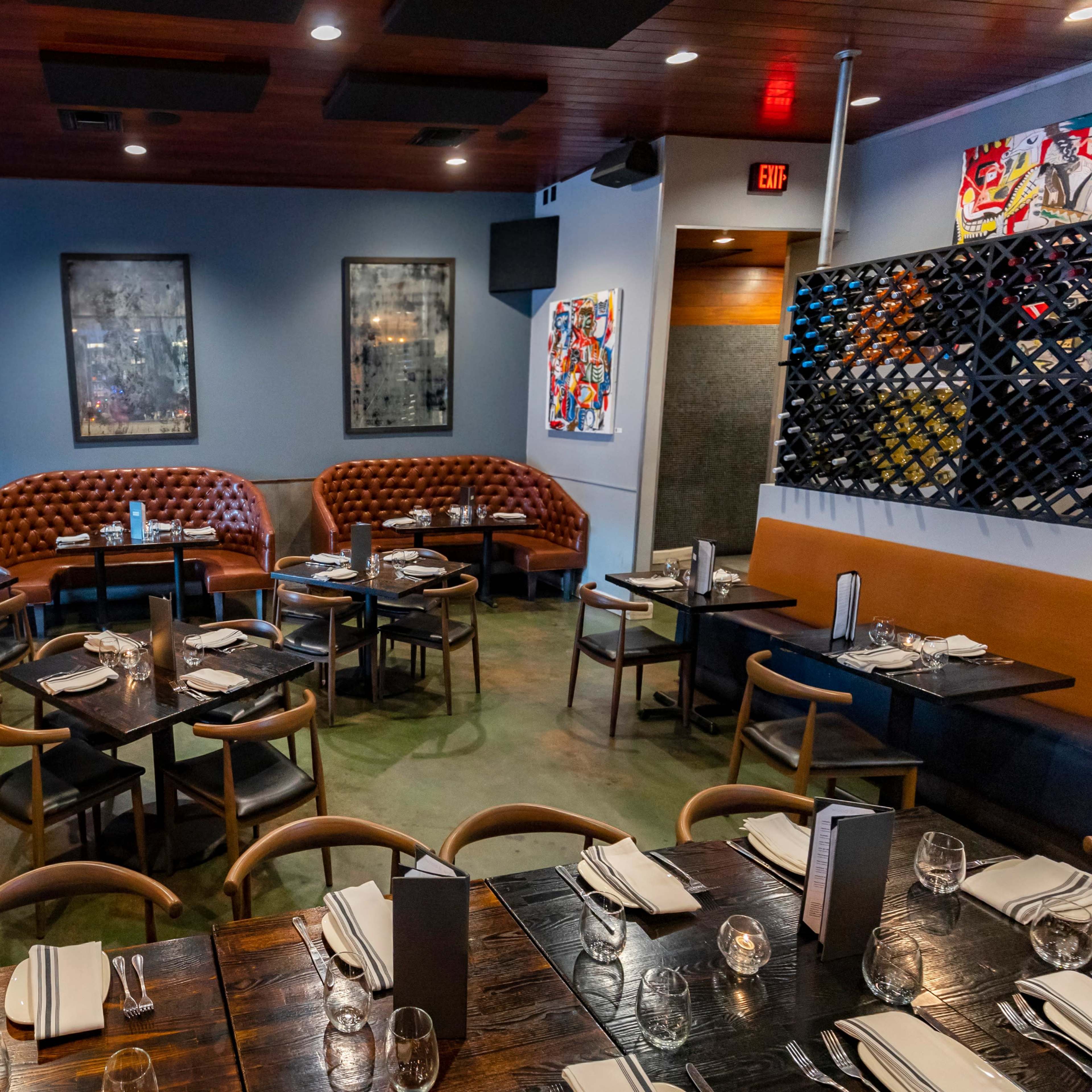 A modern restaurant interior featuring upholstered booths, a stone fireplace, and tables set for dining.