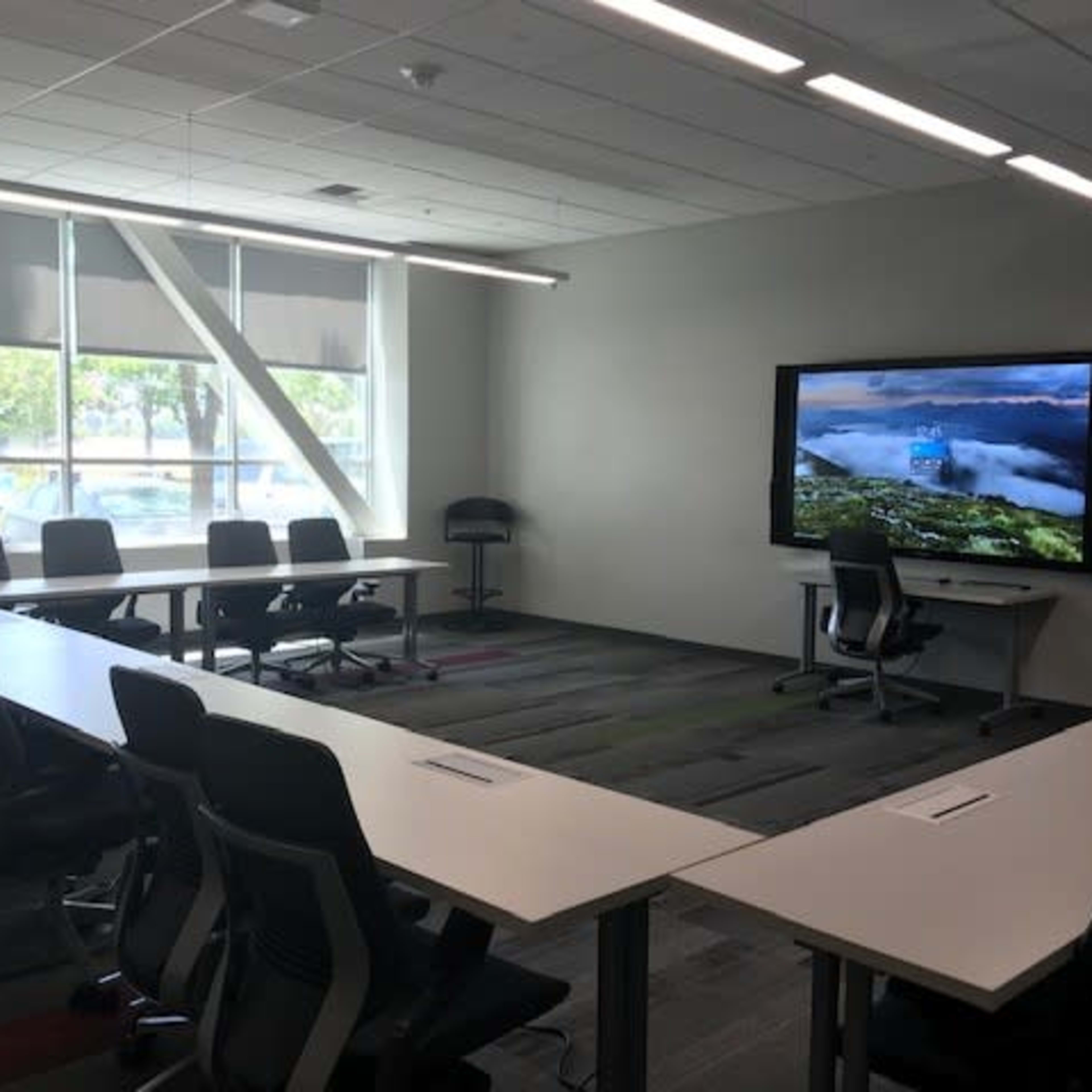 A modern conference room with several chairs and tables arranged in a U-shape around a large display screen.