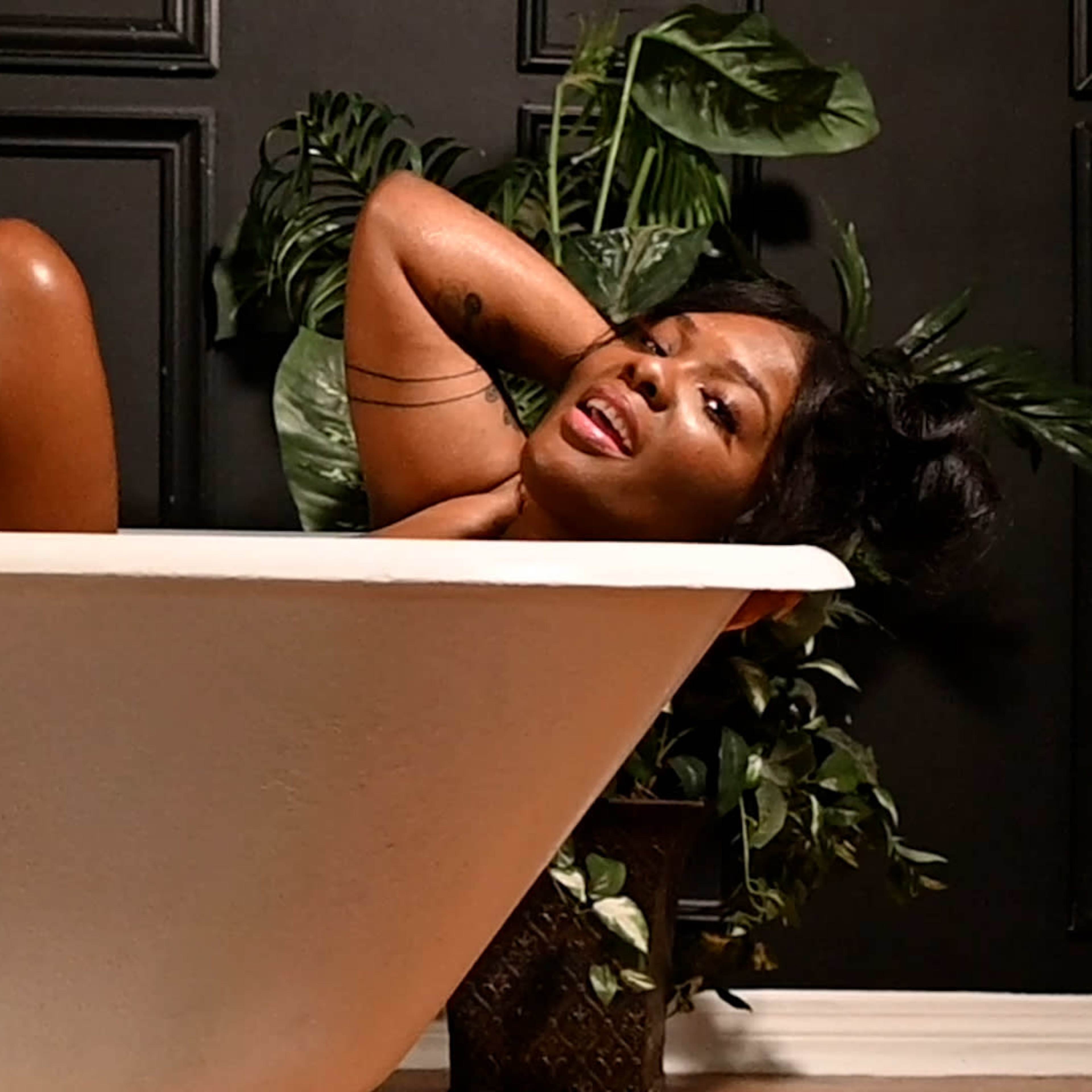 A person is partially submerged in a freestanding bathtub surrounded by indoor plants.