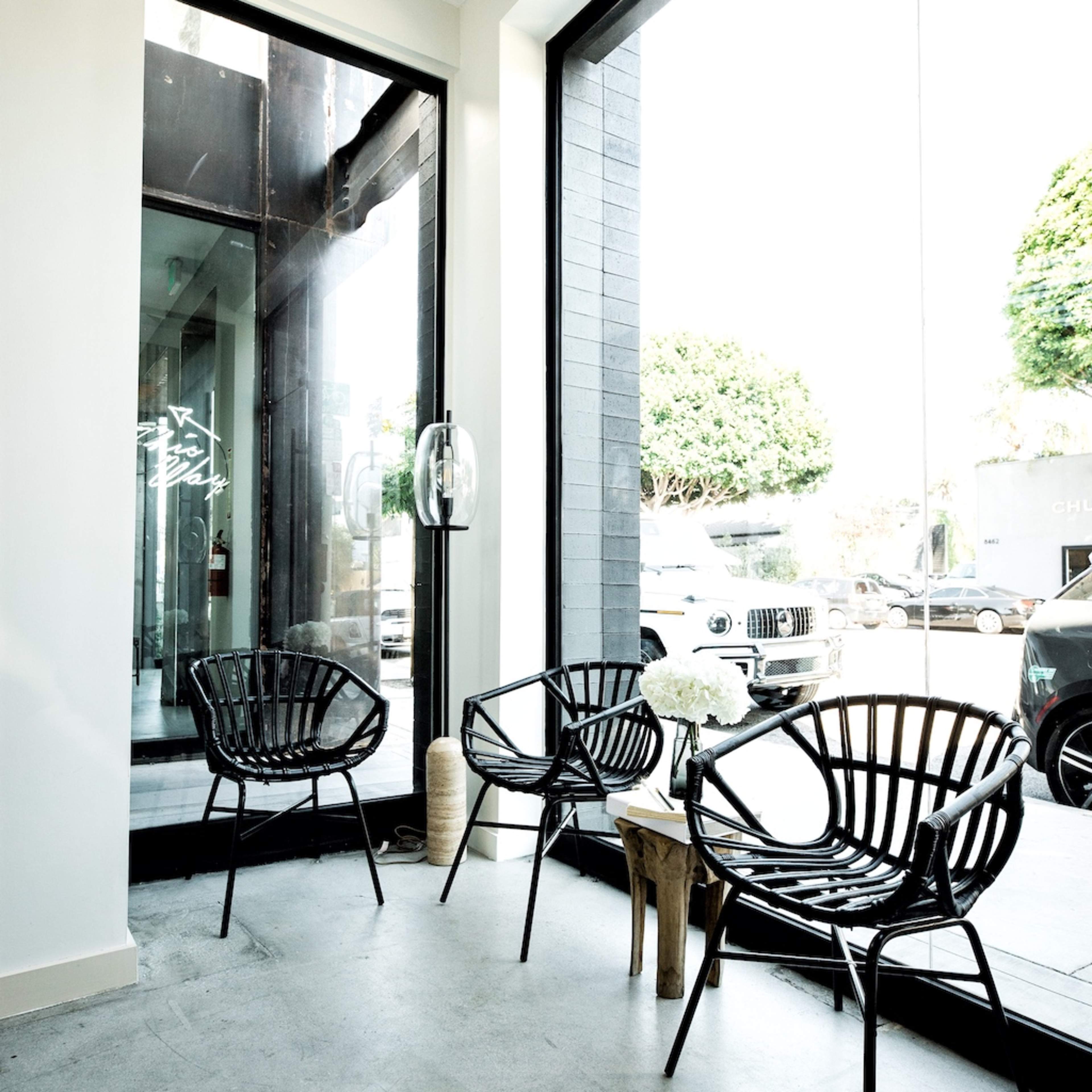 The scene features three black wire chairs positioned near a large glass window overlooking a street.
