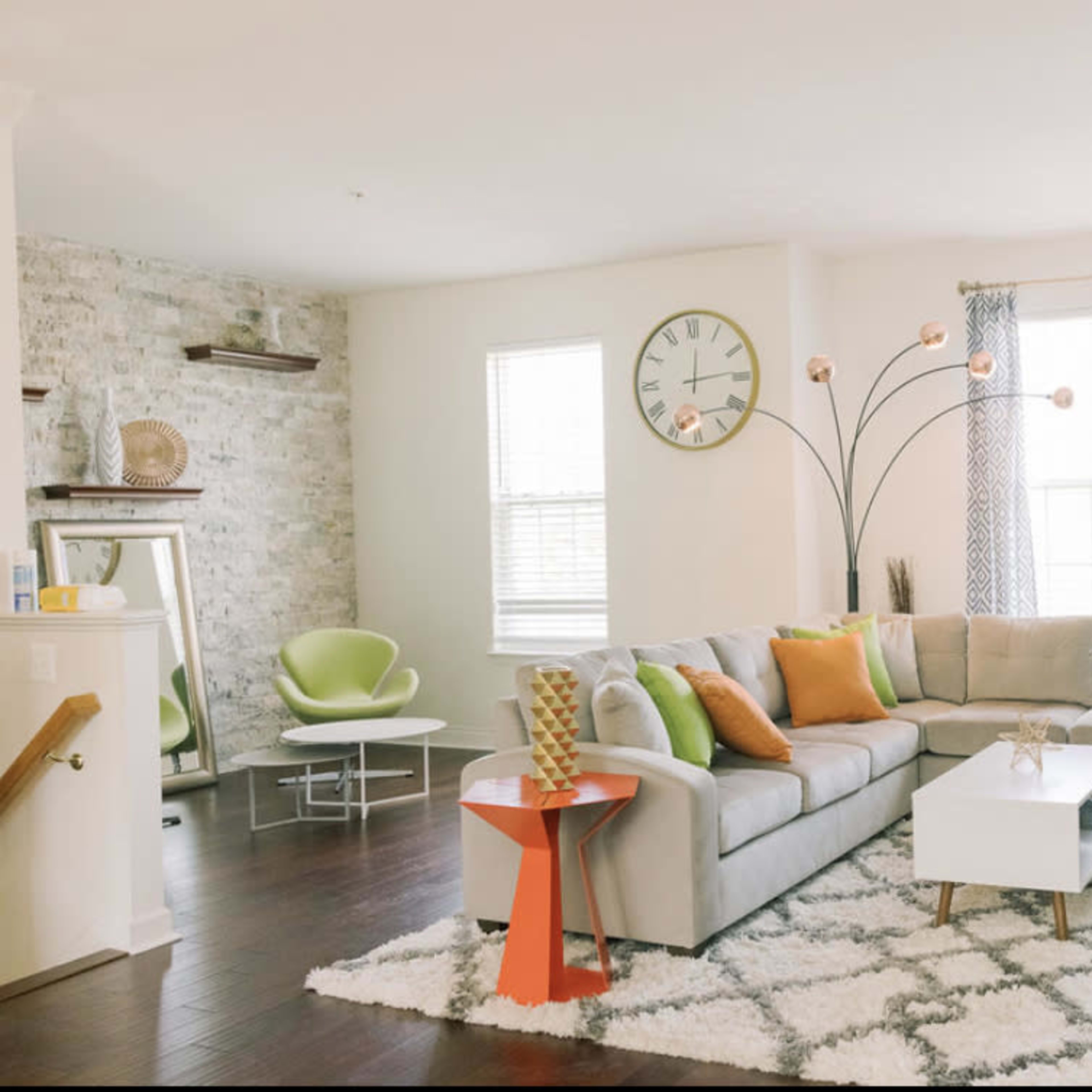 The living room features a gray sectional sofa, a white coffee table, and a decorative rug, with large windows allowing natural light and an arc floor lamp adding illumination.