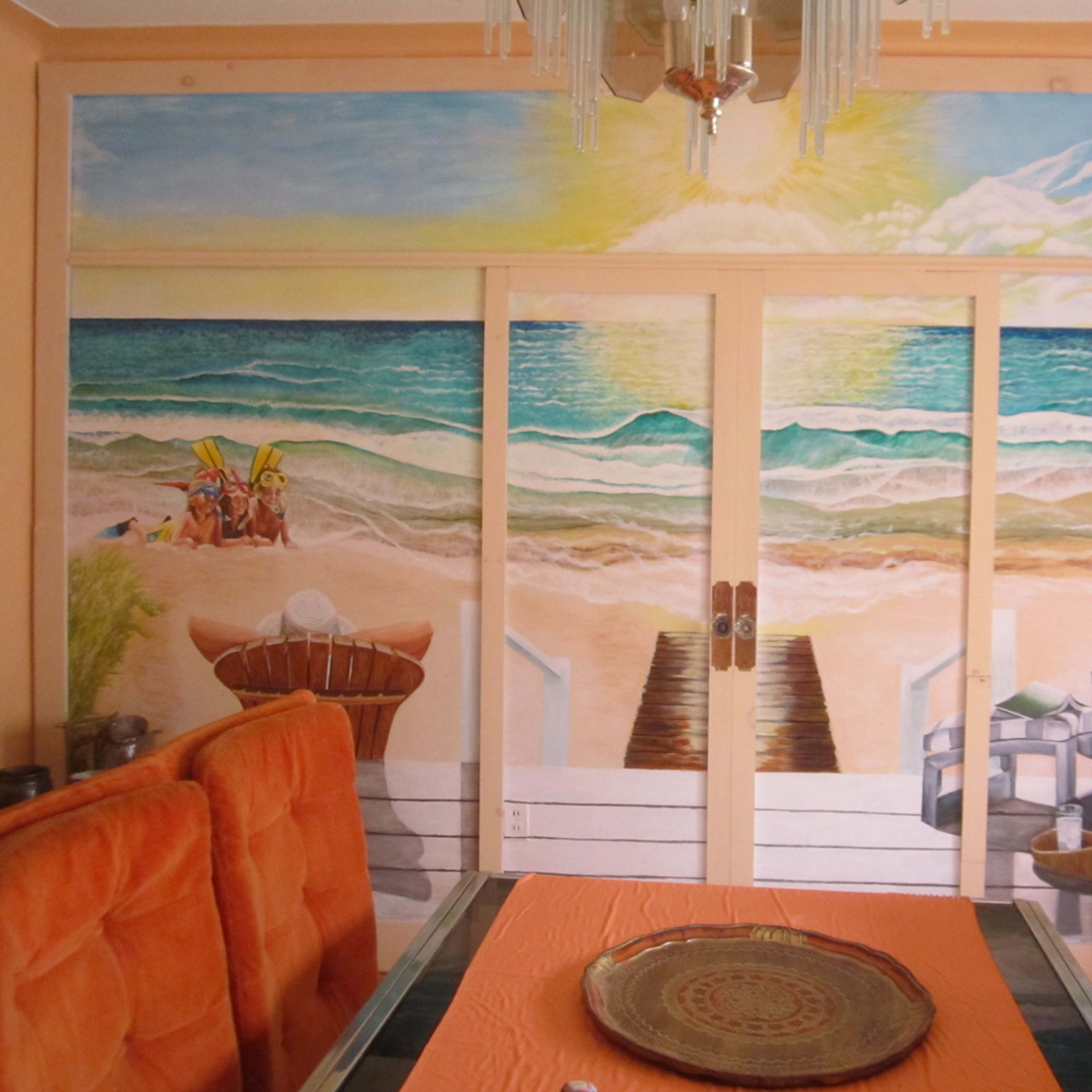A dining area with an orange table setting and a mural depicting a beach scene with waves, sand, and chairs.