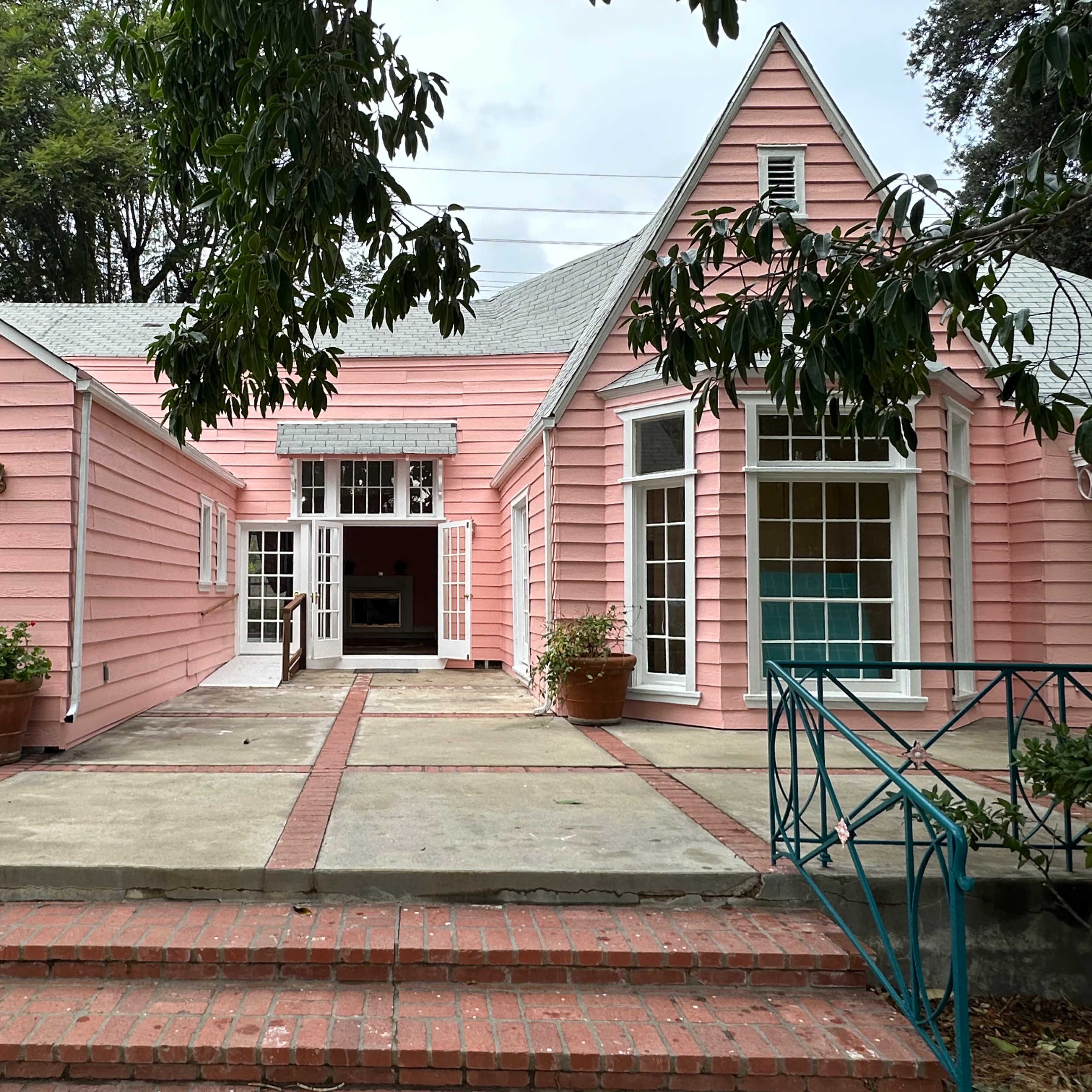 A pink house with a triangular roof, large windows, and a brick pathway leading to its entrance.