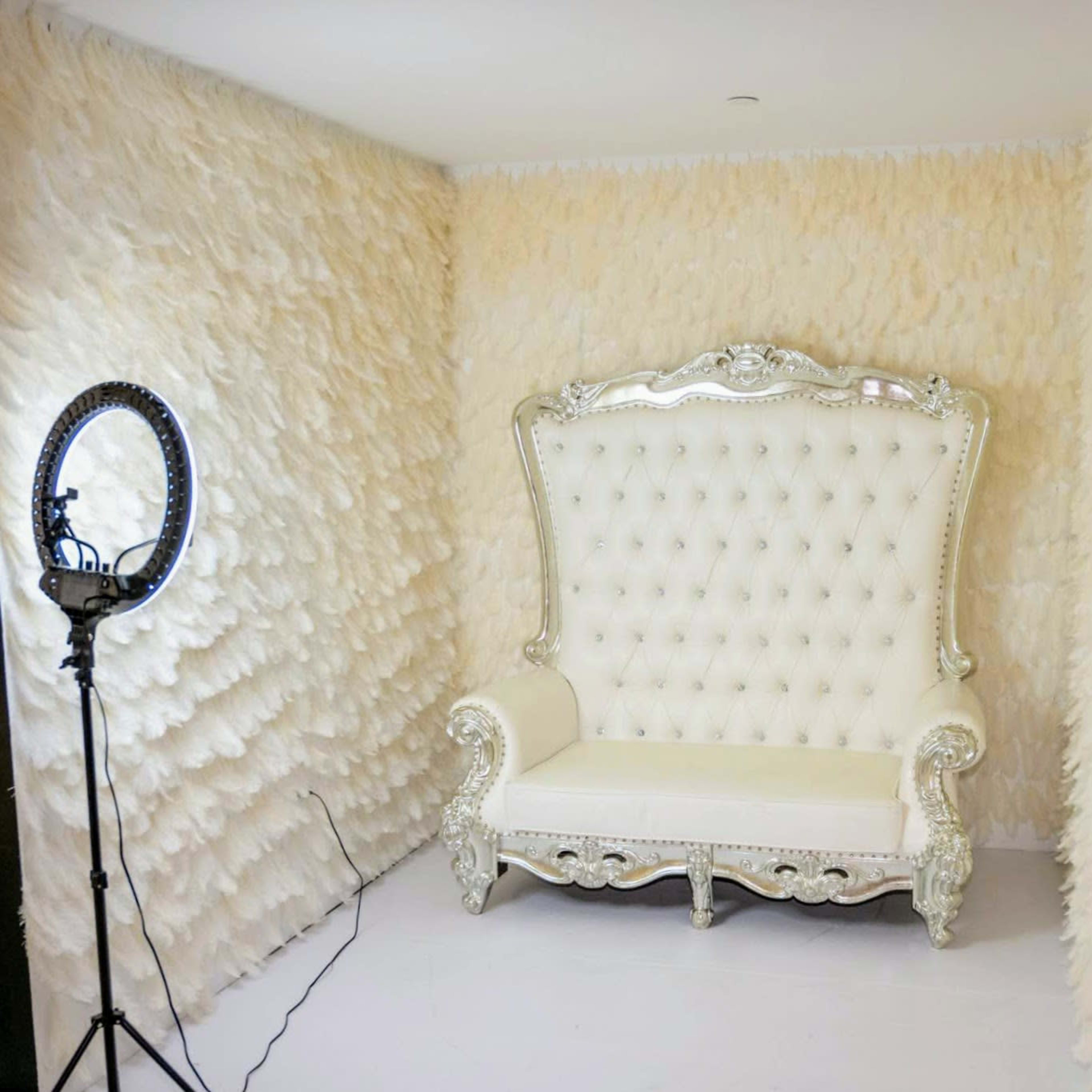 A luxurious white tufted sofa with ornate silver detailing, positioned in a room with textured, pale beige walls.