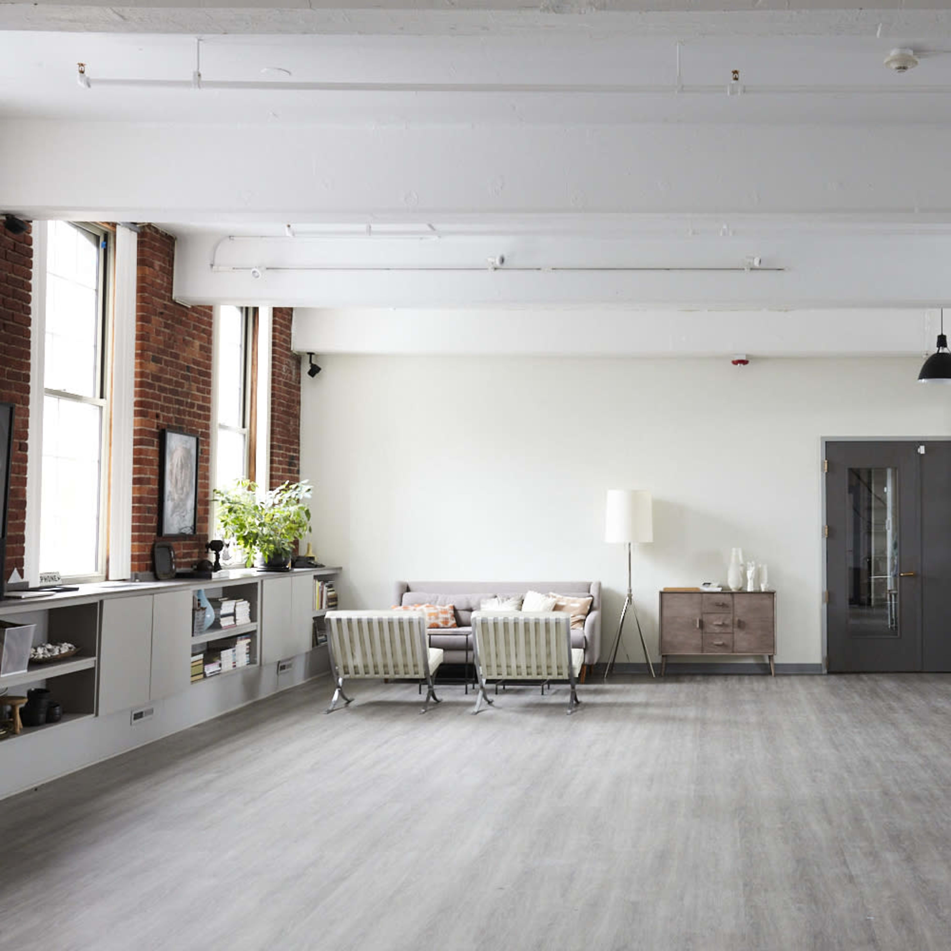 A spacious, minimalistic loft features large windows, a modern sofa, a wooden cabinet, and an open kitchen area with a dining table.