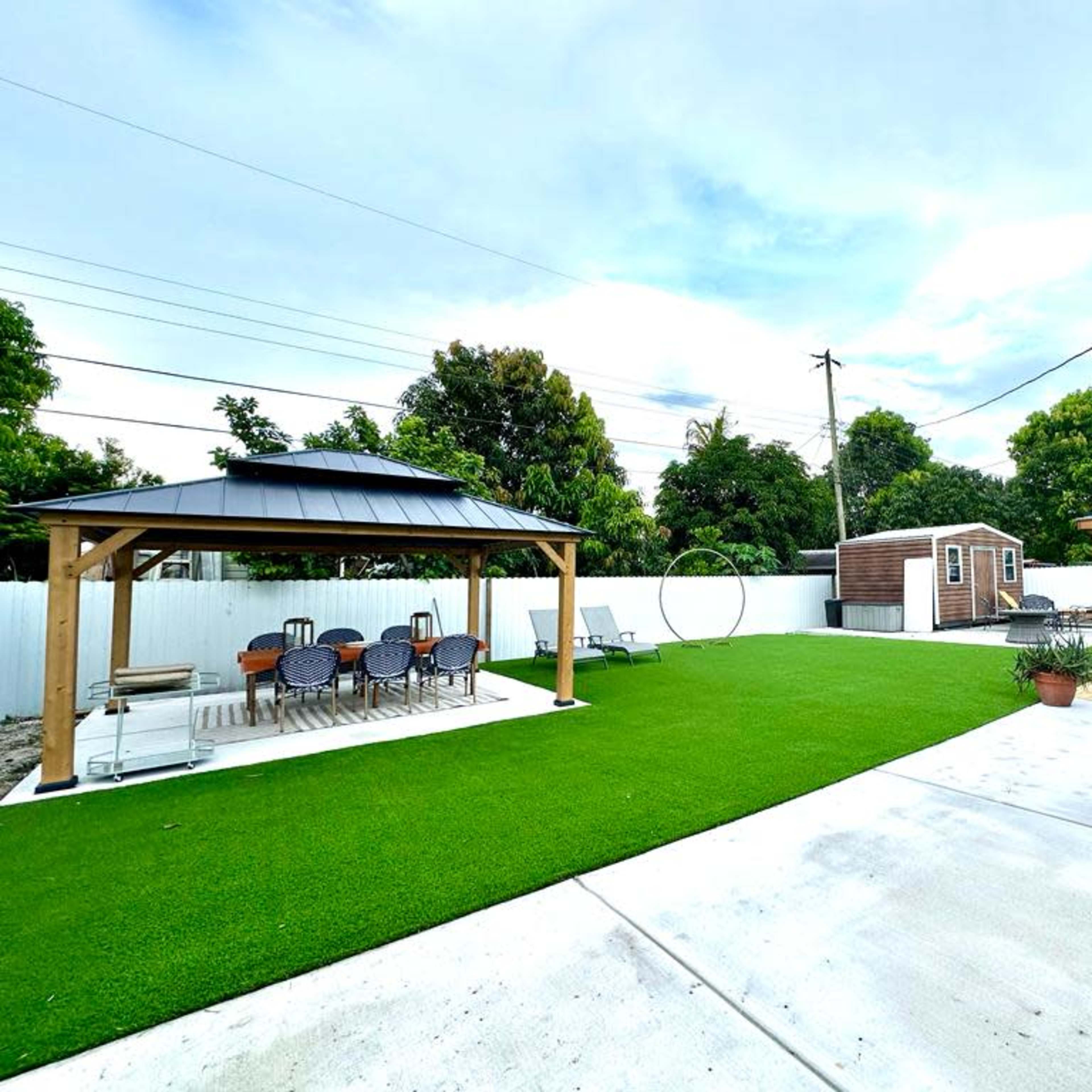 A landscaped backyard featuring two wooden gazebos, a patch of artificial turf, and a storage shed in a fenced area.