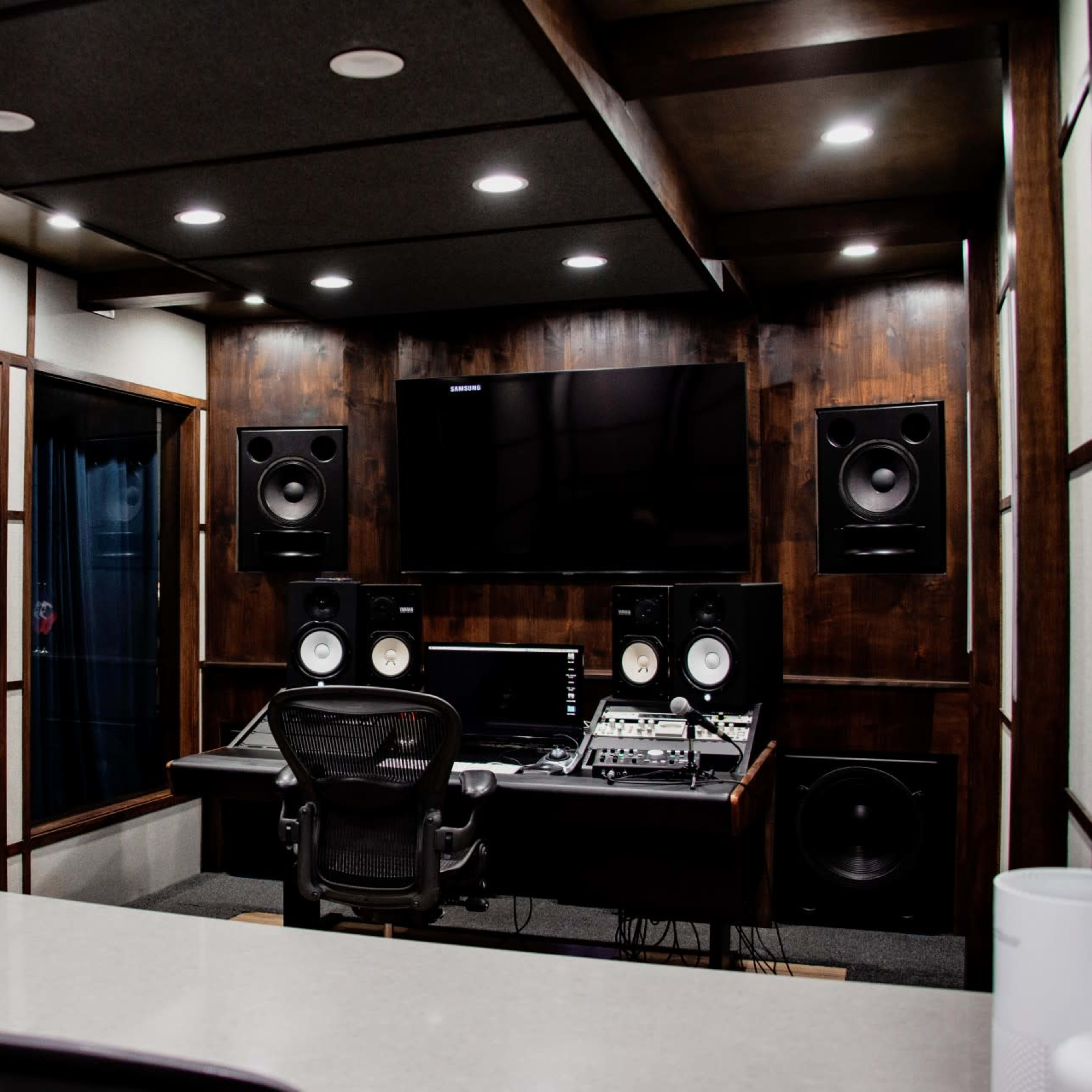 A modern recording studio features dark wood paneling, a soundproof design, and professional audio equipment.