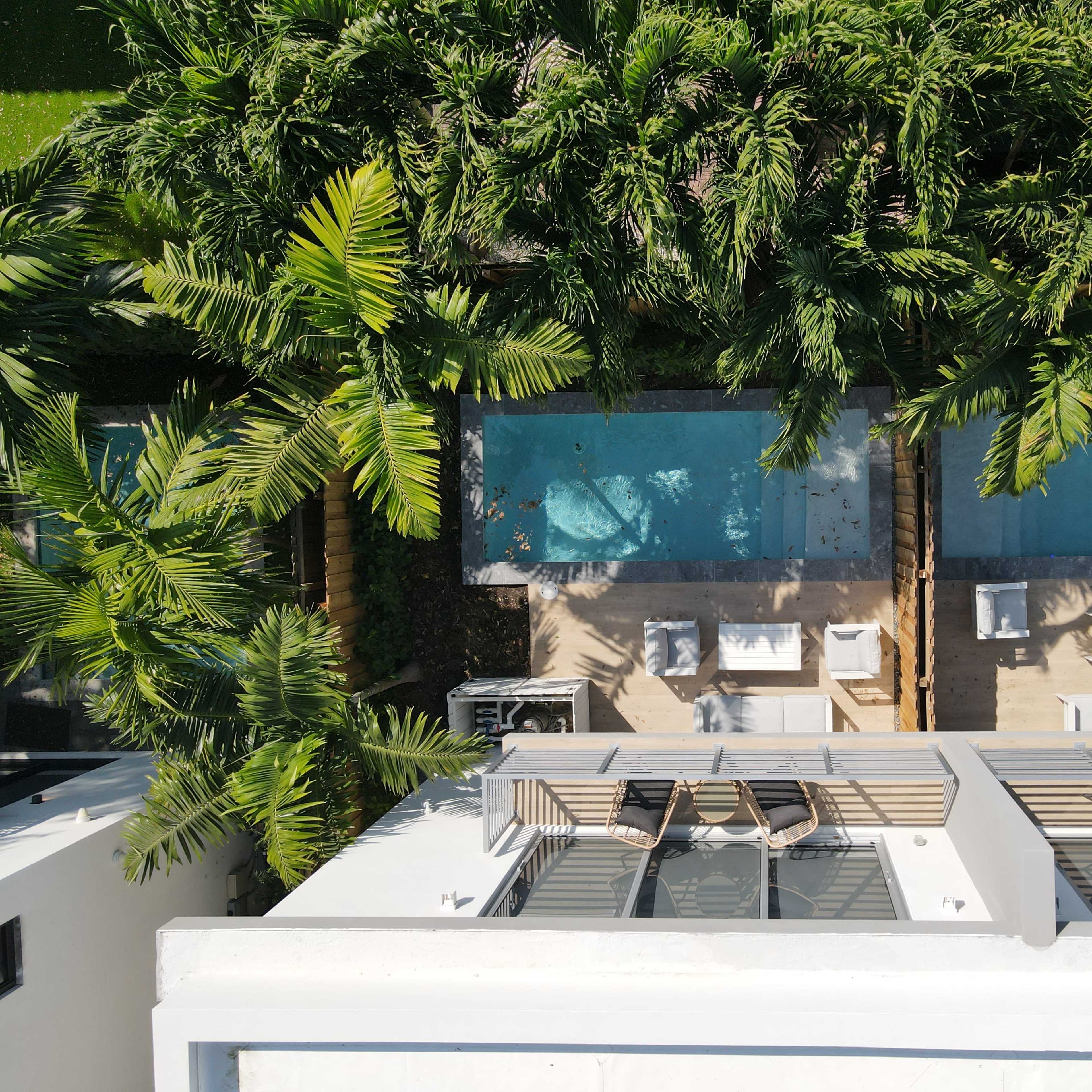 A bird's-eye view of two swimming pools surrounded by palm trees and lounge chairs on a modern rooftop.