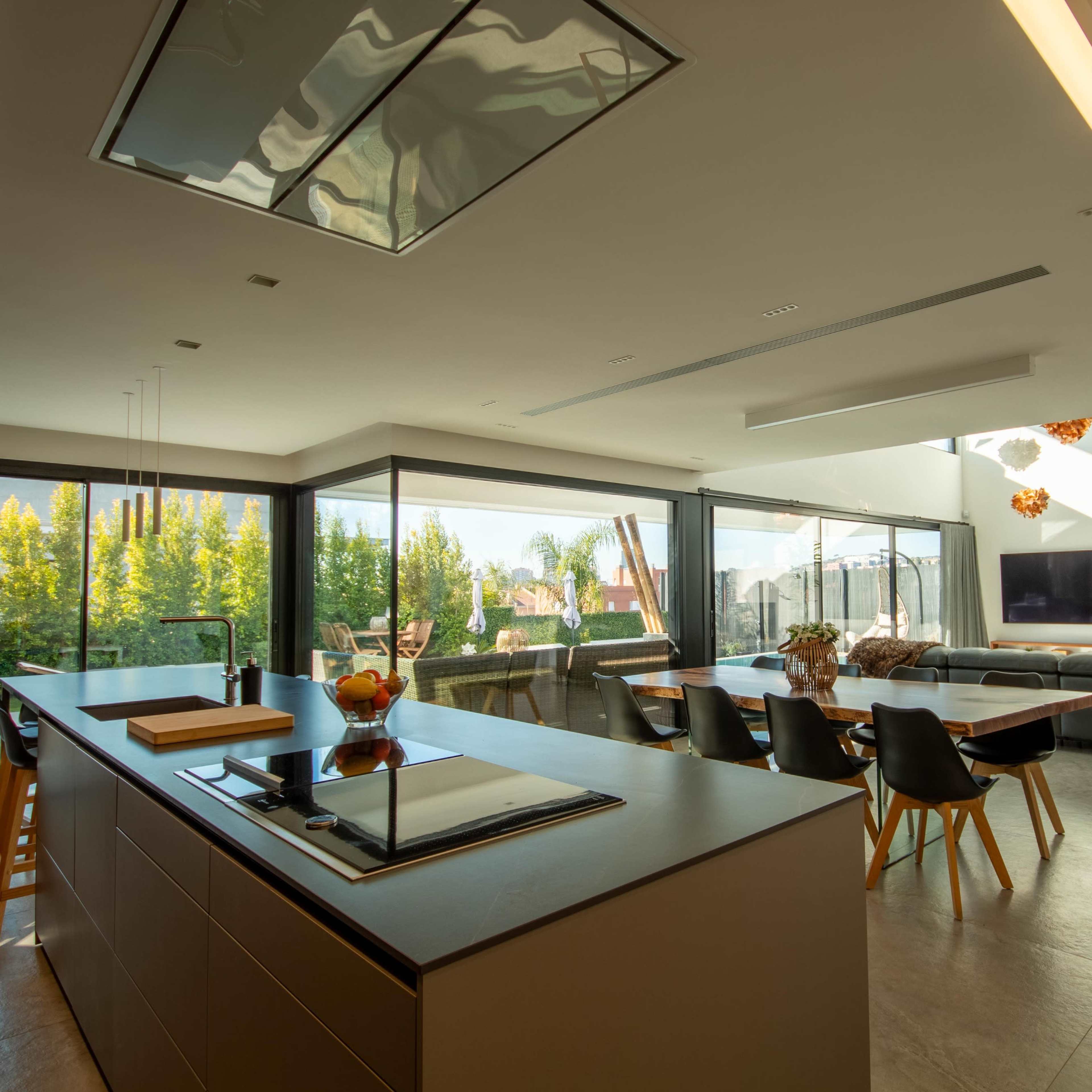 A modern open-concept kitchen and living area with large windows overlooking a green landscape.
