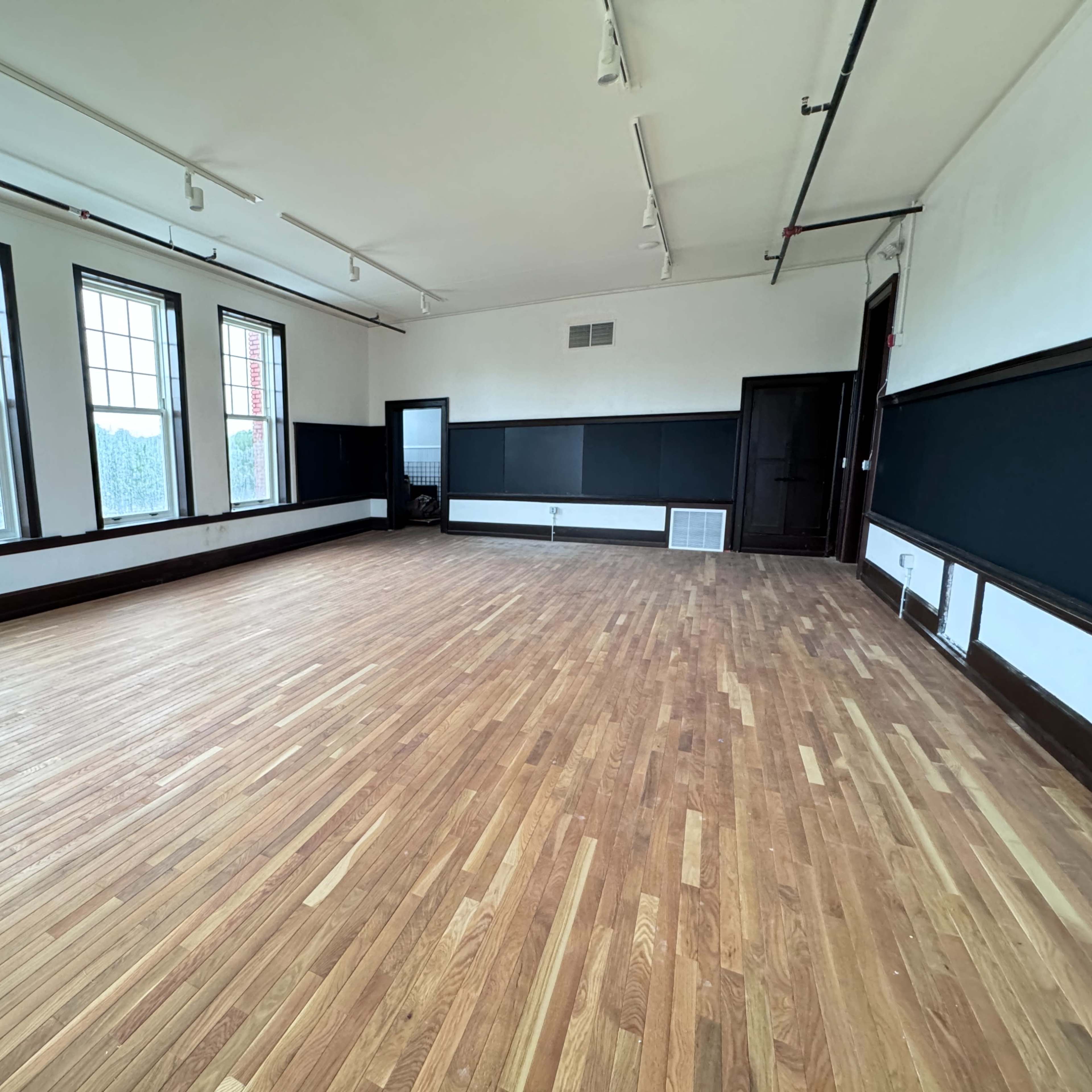 A spacious, empty room with hardwood floors and large windows along the walls.
