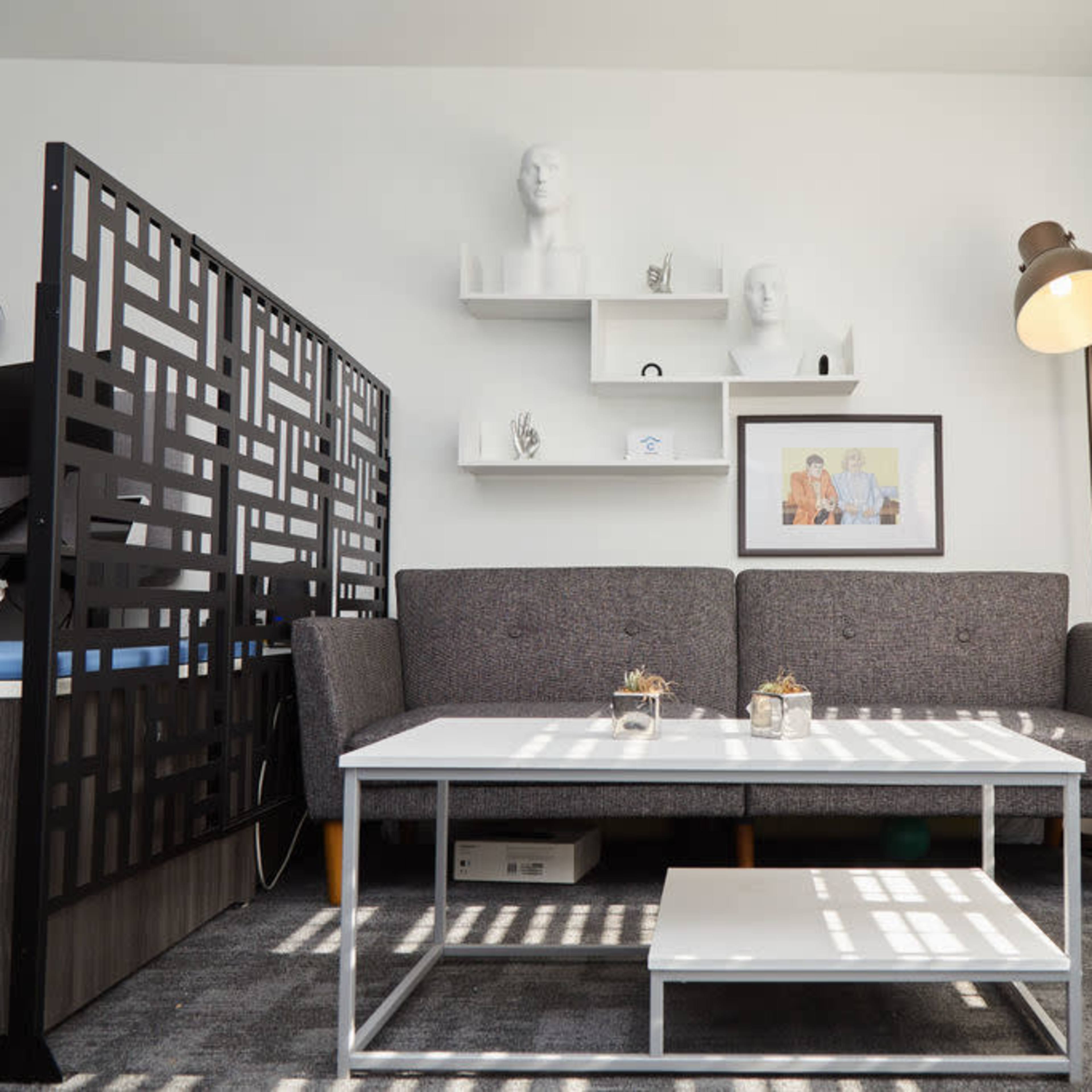 A modern living room with a gray sofa, a coffee table, and decorative shelves featuring sculptures and framed artwork.