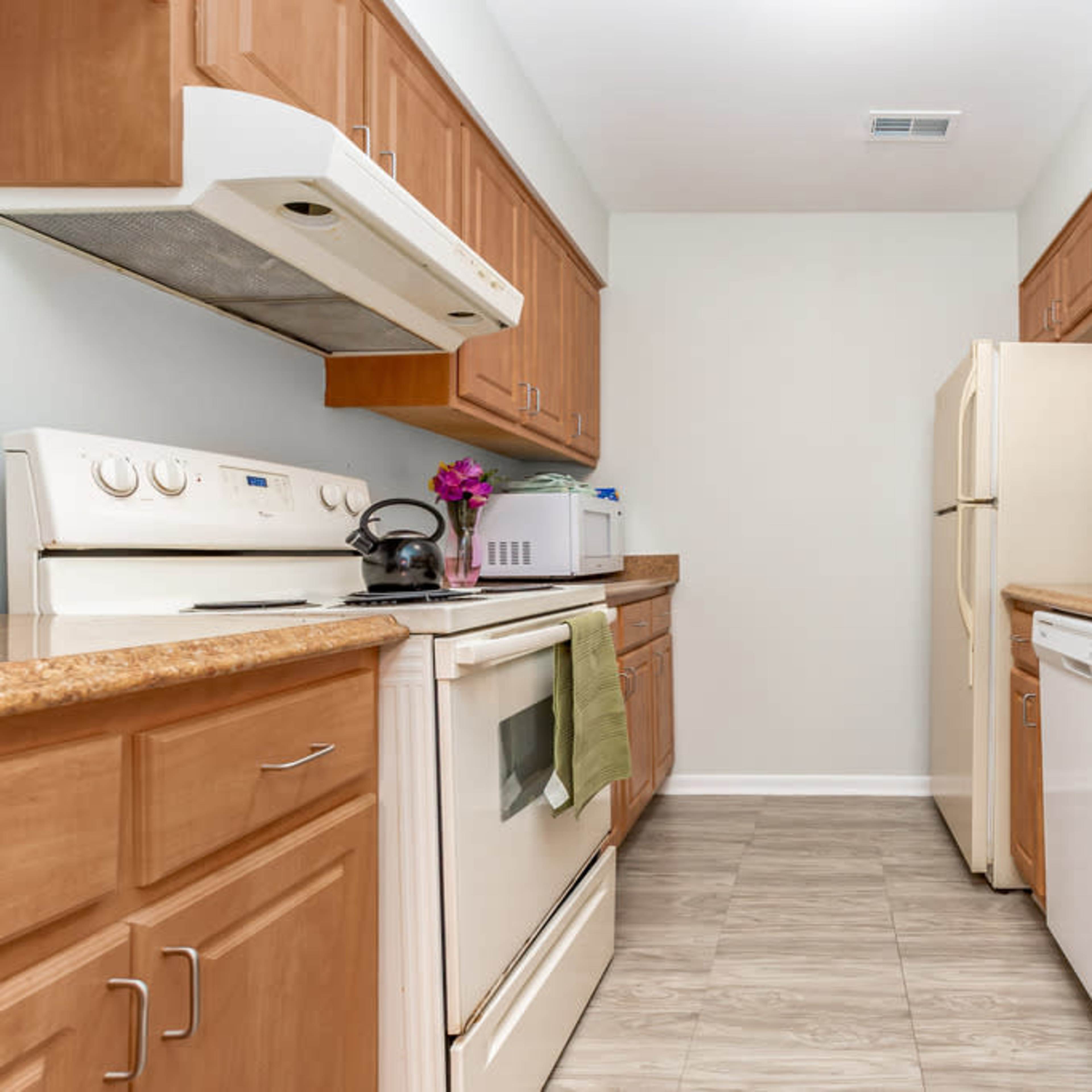 A kitchen with wooden cabinets, a white oven, and a refrigerator, featuring a counter space and a sink.