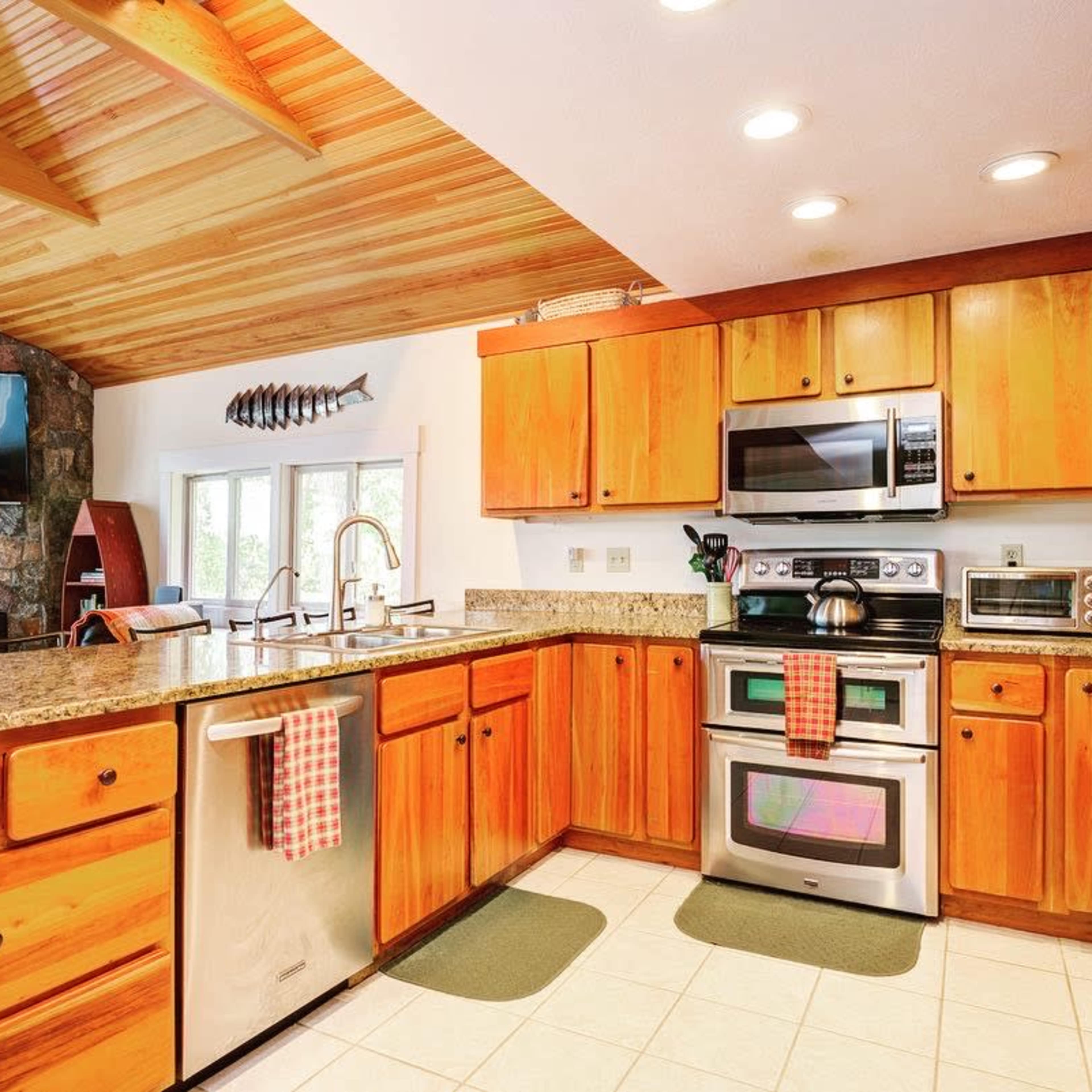 The kitchen features wooden cabinets, stainless steel appliances, and a granite countertop beneath a vaulted ceiling with exposed beams.