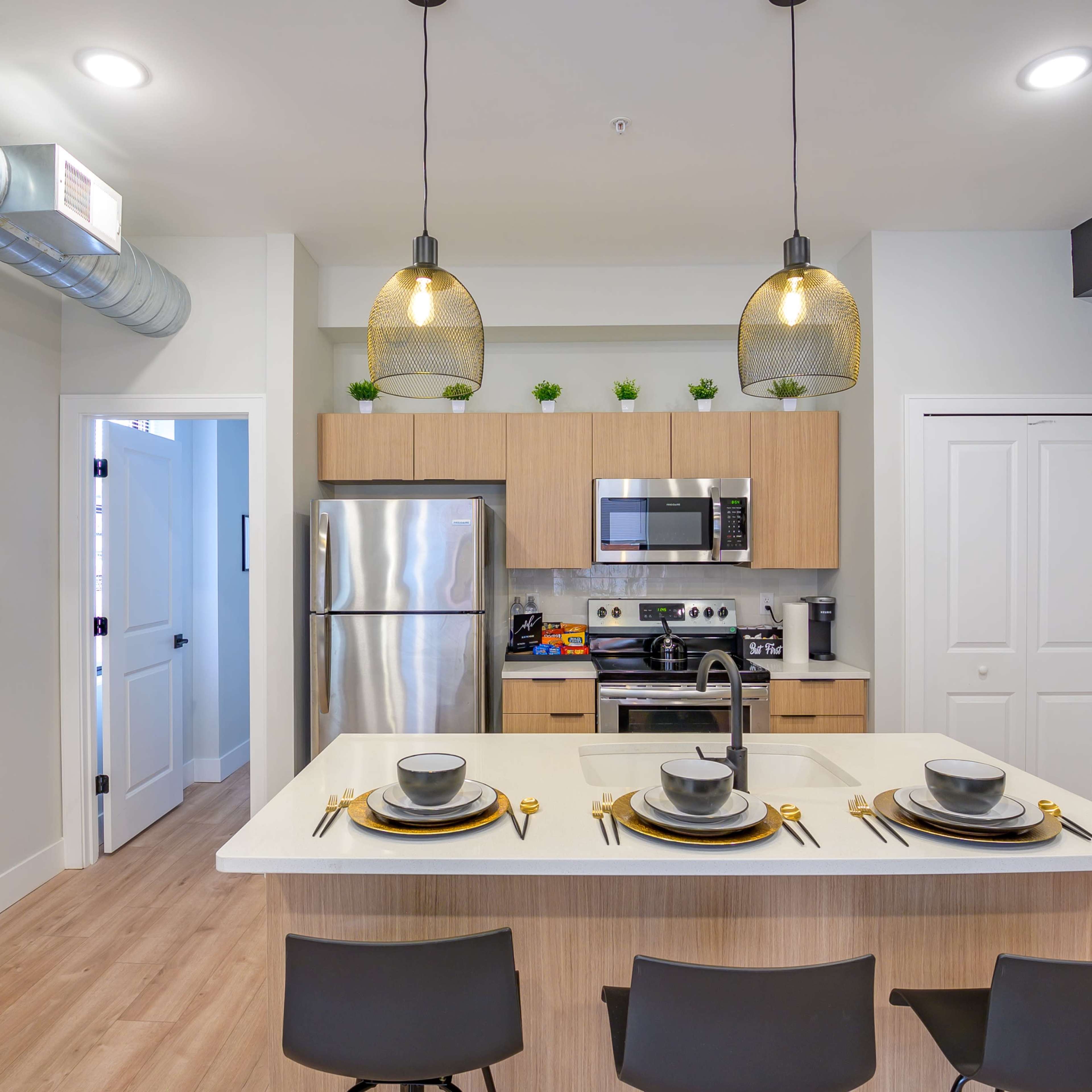 A modern kitchen with a dining area featuring a central island, stainless steel appliances, and three place settings.