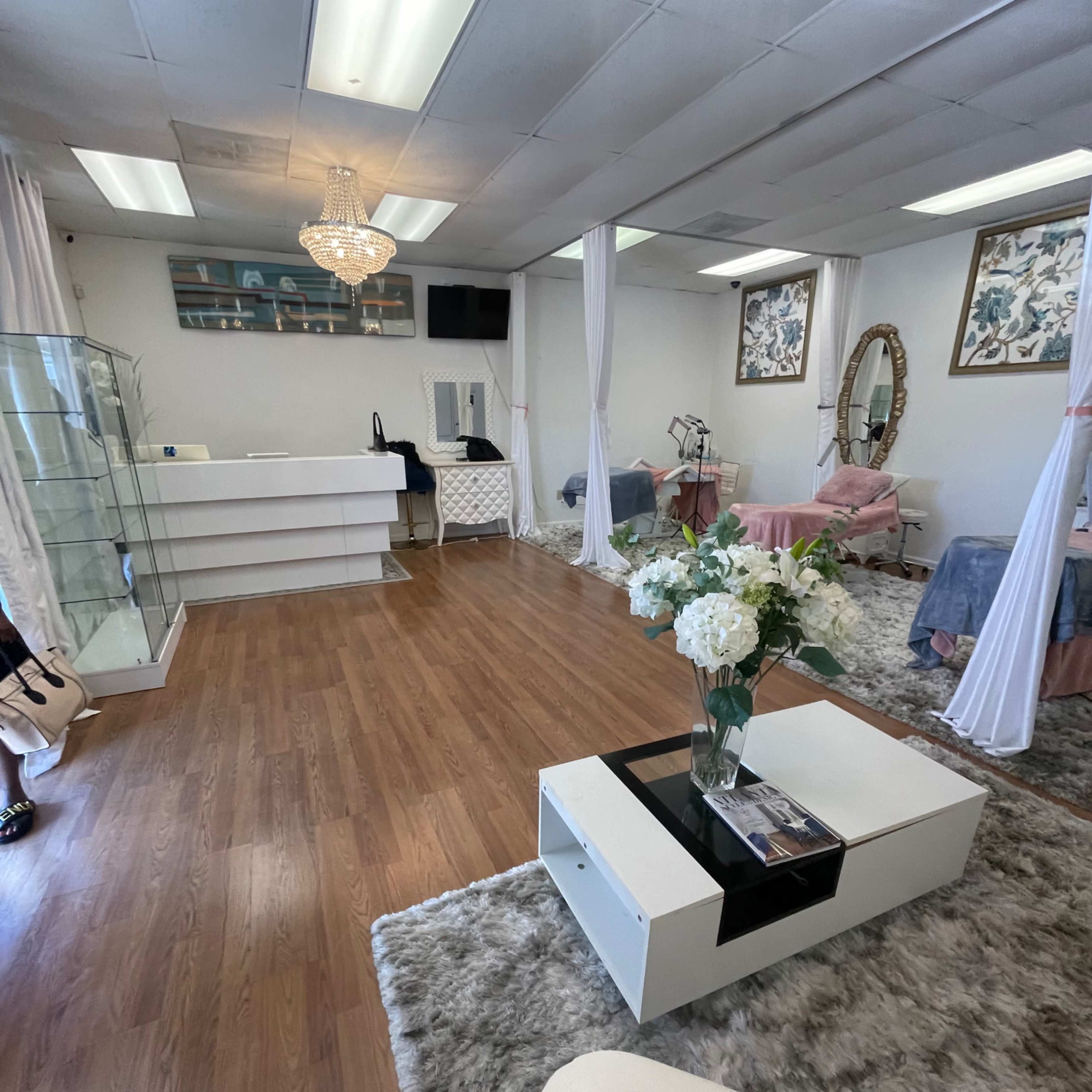 A clean, well-organized salon interior with wooden flooring, soft seating, display cases, and floral arrangements.