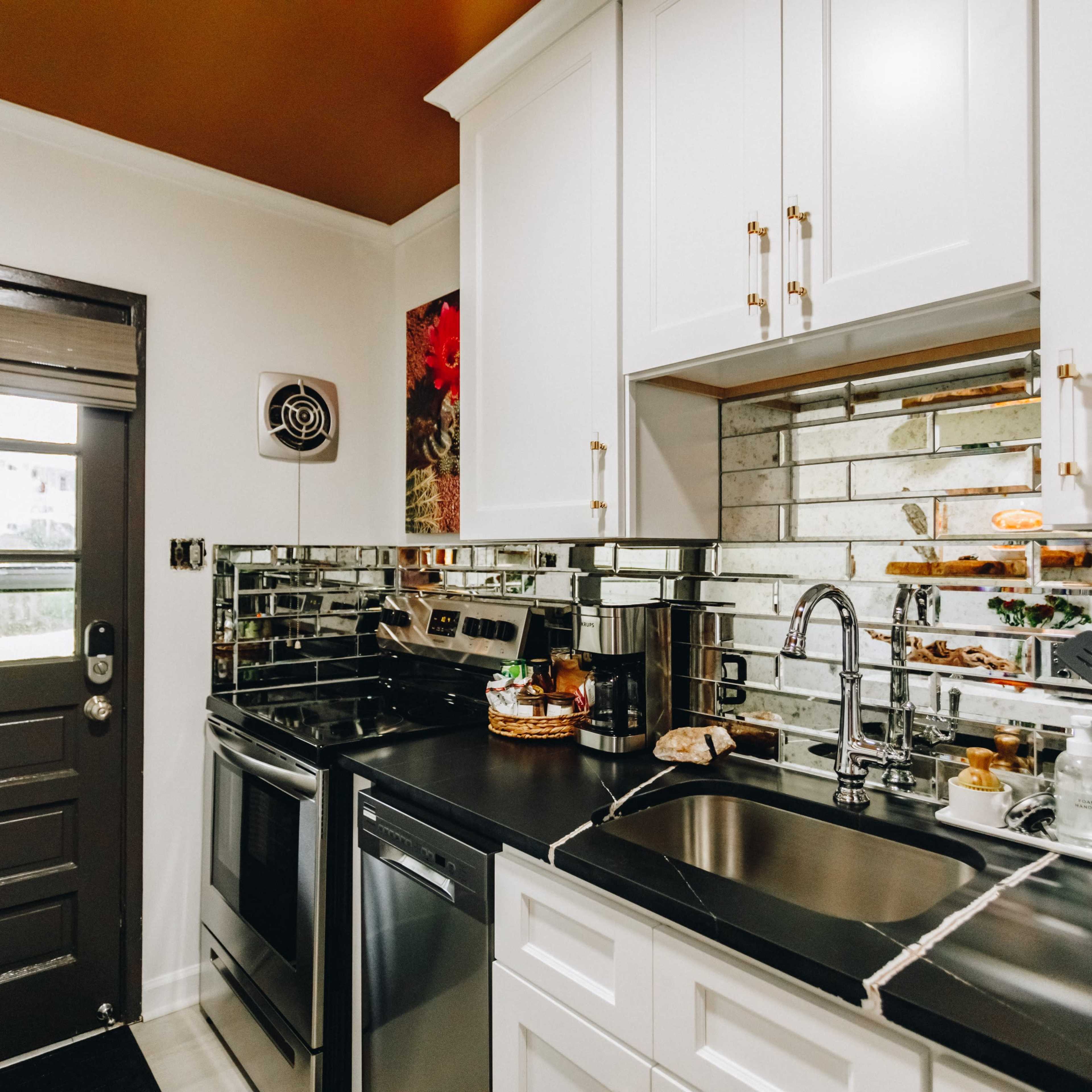 The kitchen features white cabinetry, mirrored backsplash, stainless steel appliances, and a dark countertop, with a door leading outside.
