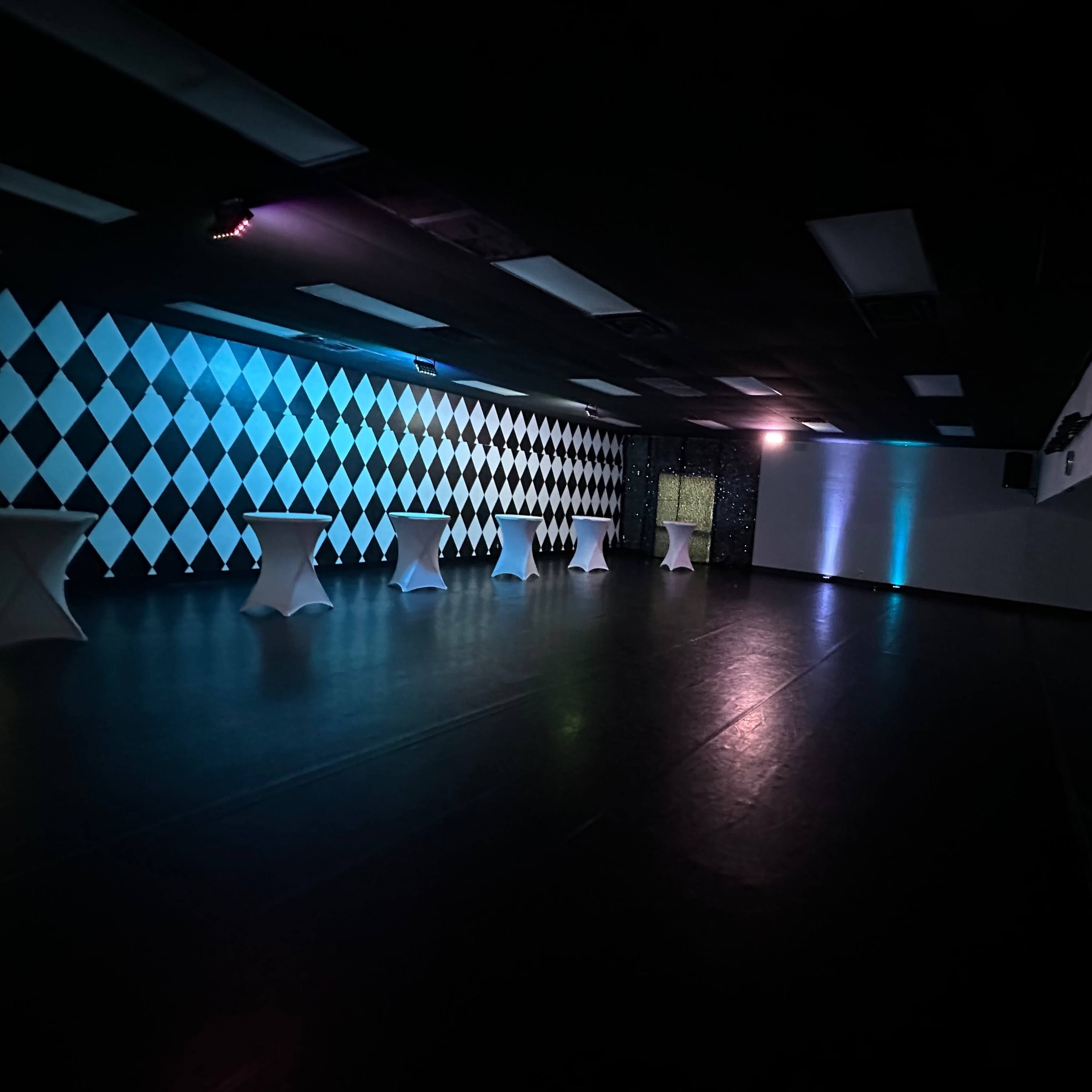 An empty event space with a checkered wall and illuminated tables.