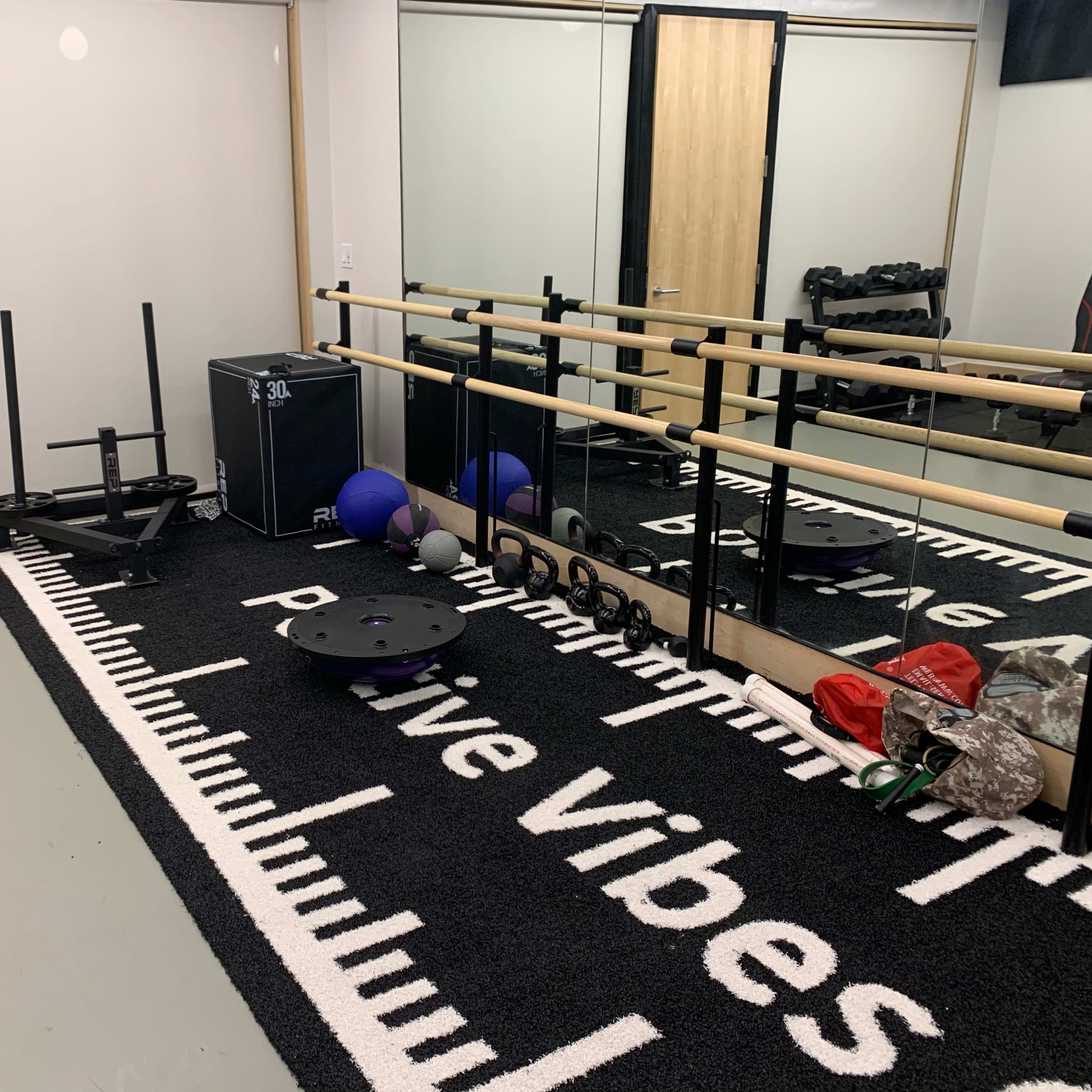 A small gym area with a black and white rug, exercise equipment including weights, a sled, and a mirror along one wall.
