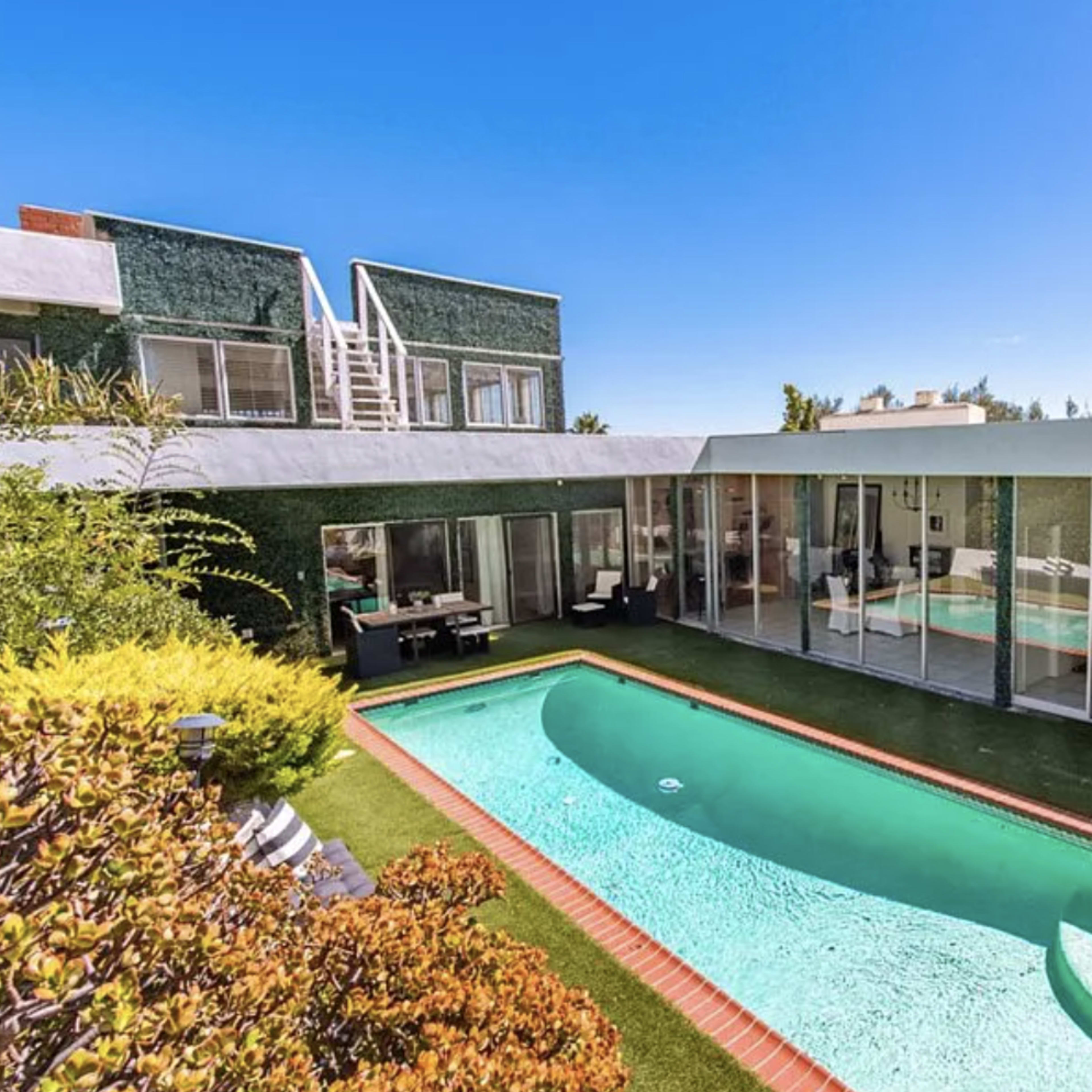 A modern home with a glass facade and a rectangular swimming pool surrounded by landscaped greenery.