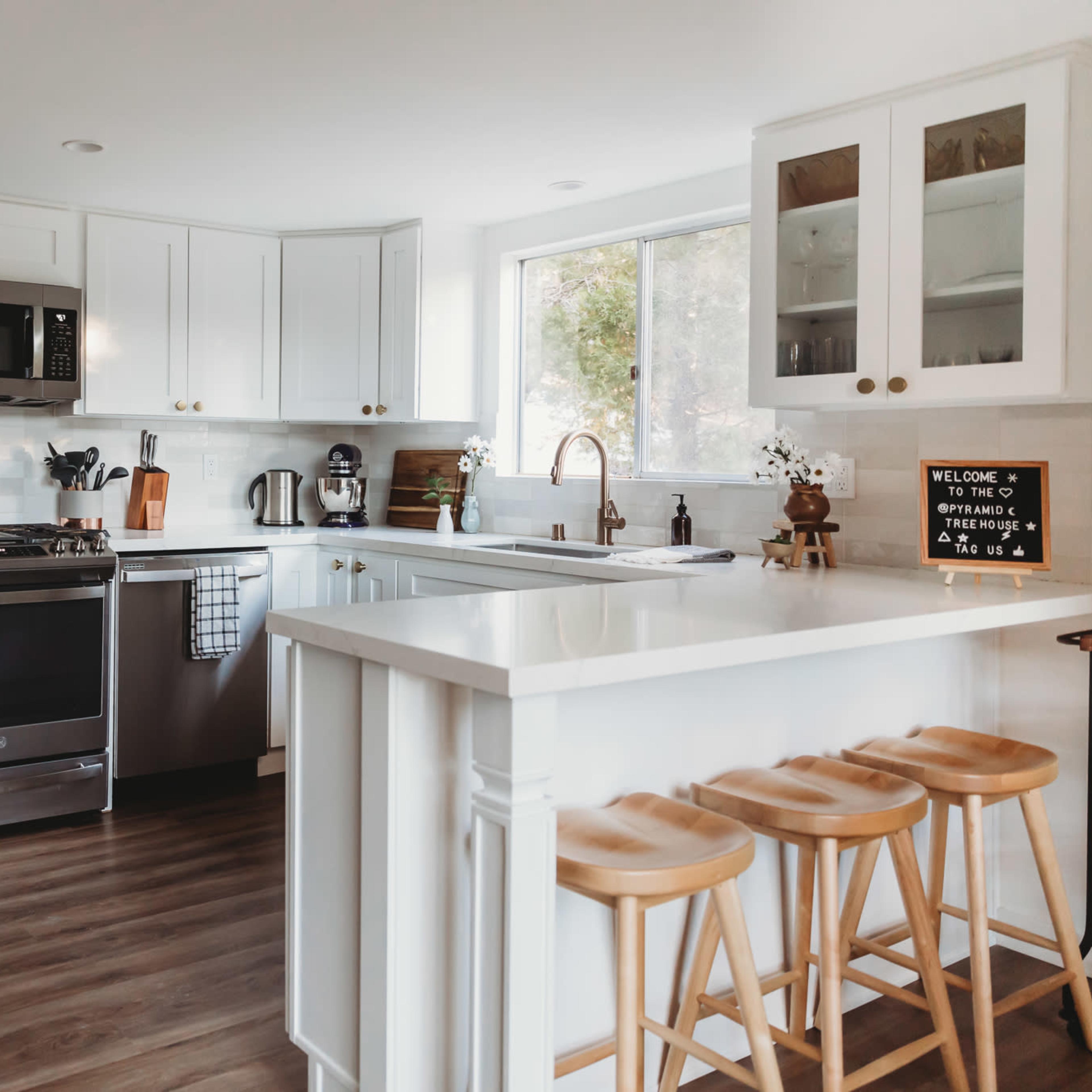 A modern kitchen features stainless steel appliances, white cabinetry, and a bar area with four wooden stools.