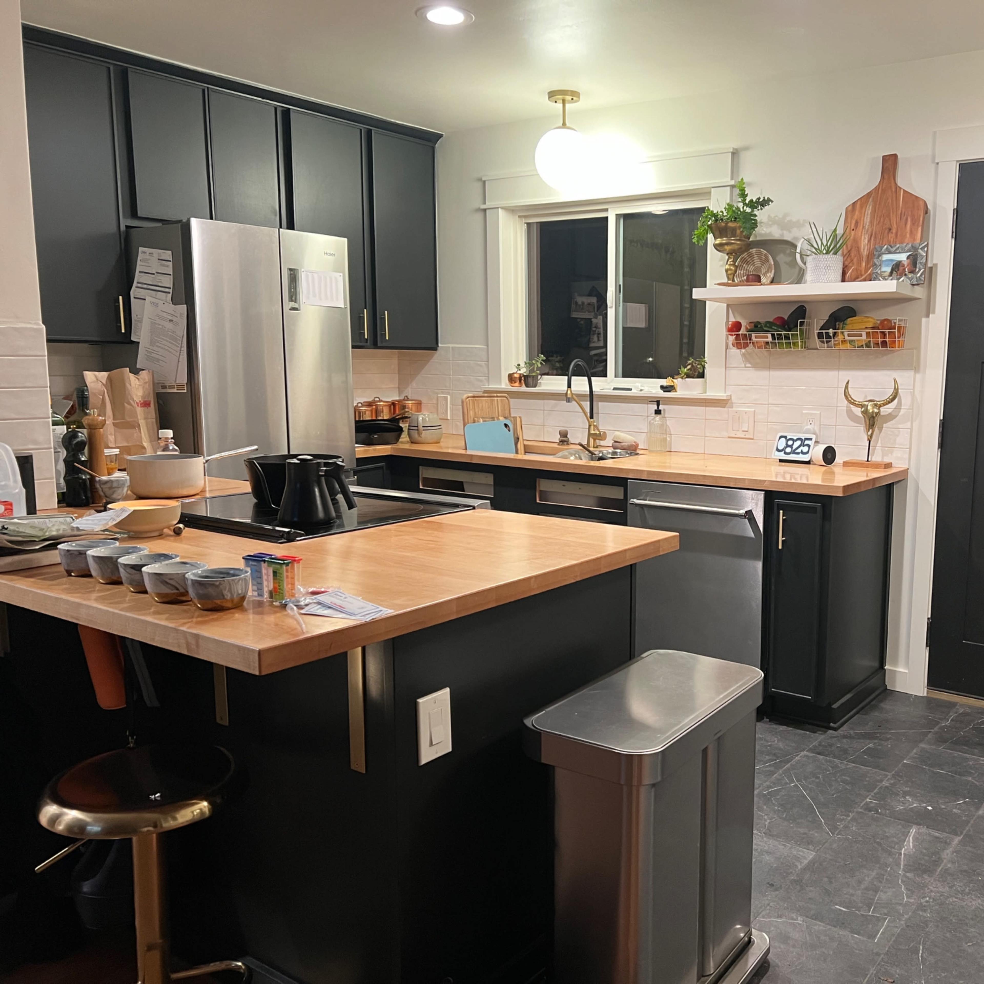 A modern kitchen with black cabinets, a wooden countertop, stainless steel appliances, and an adjacent door leading outside.