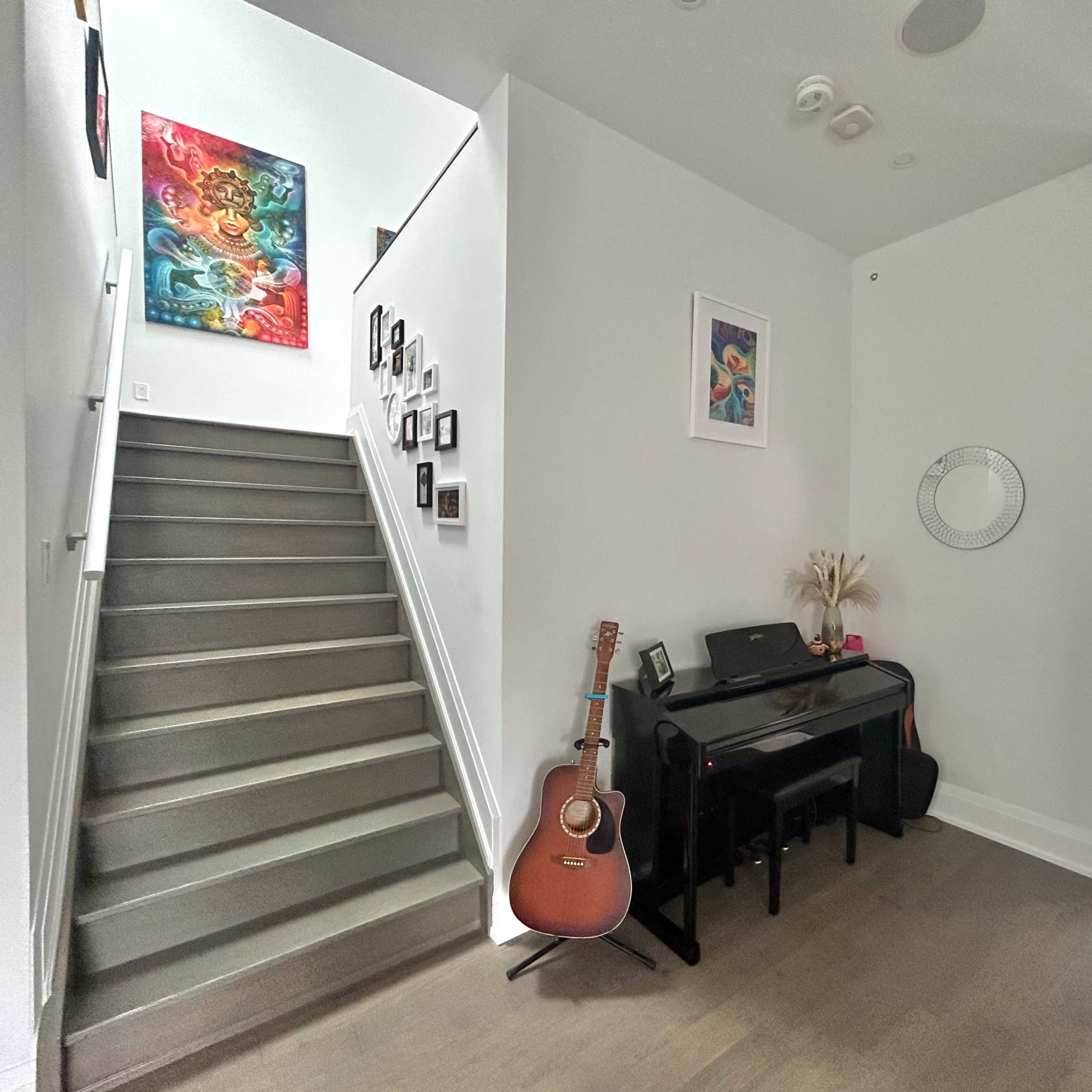 A modern foyer with a staircase on the left, a piano and guitar on the floor, and artwork on the walls.