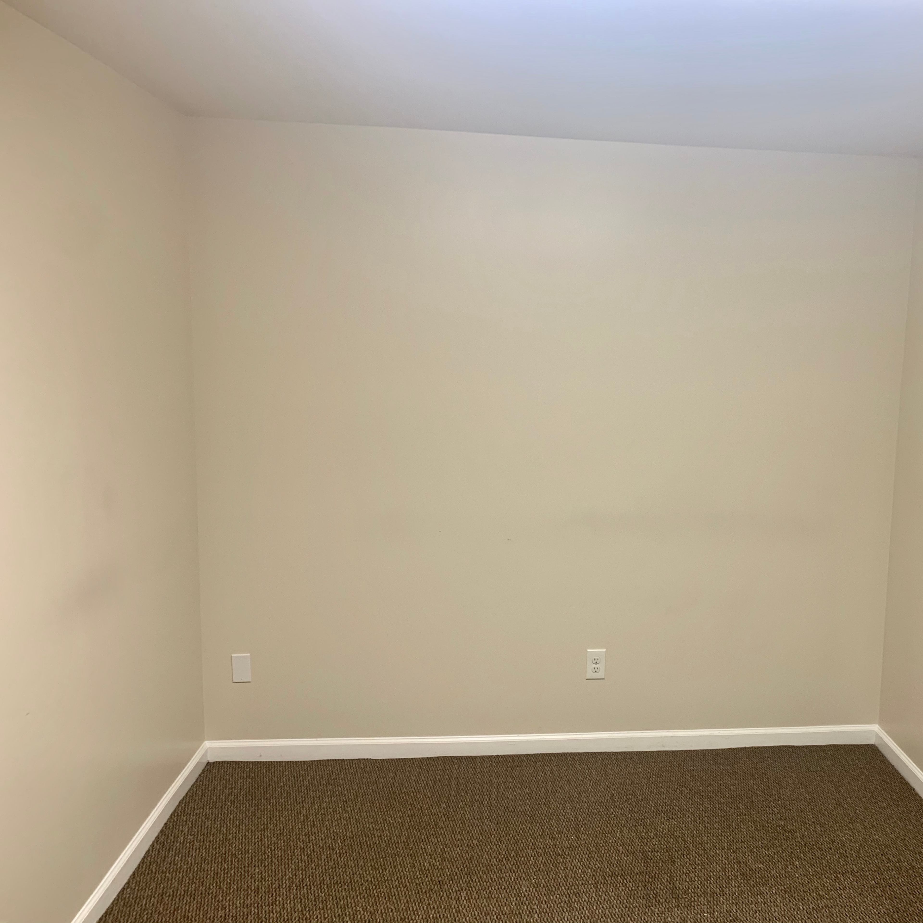 An empty room with beige walls and a carpeted floor, featuring a keyboard on the right side.