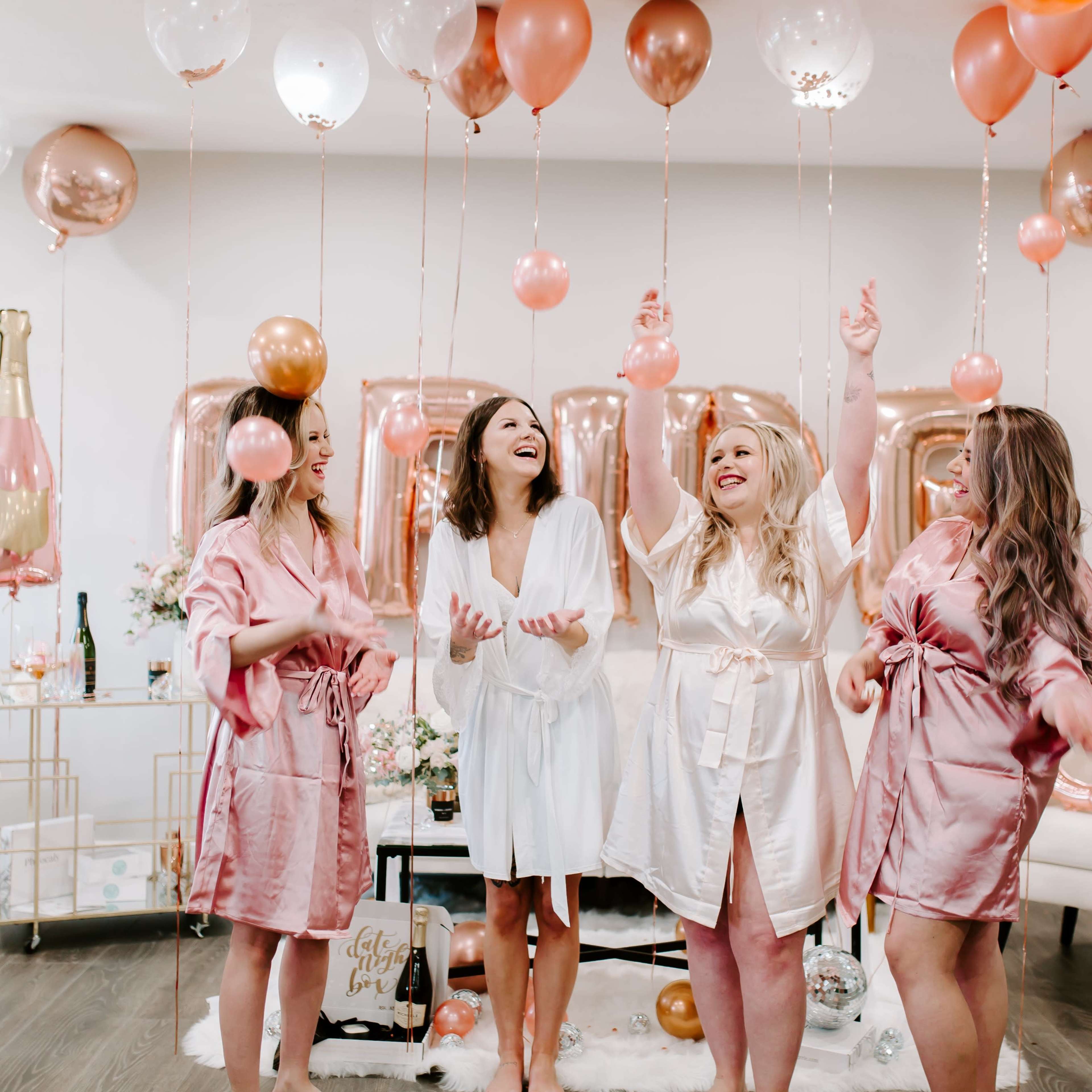 Four women in robes celebrate with balloons in a decorated room.