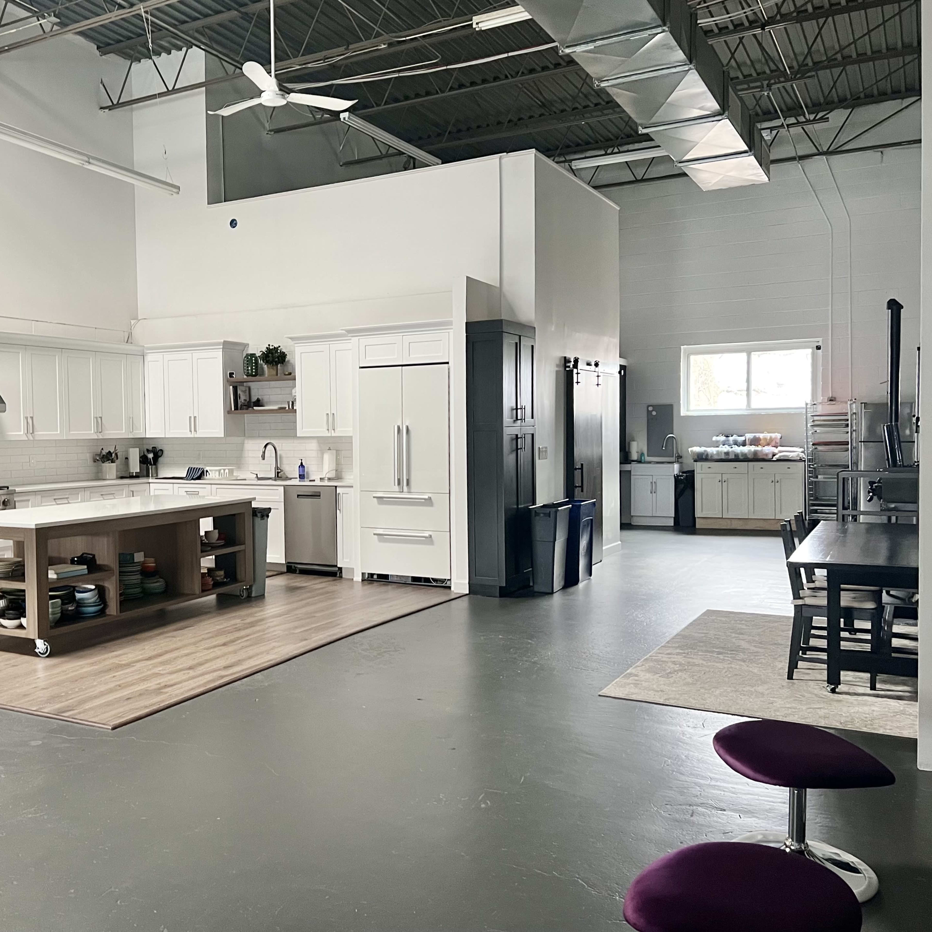 A spacious industrial kitchen with modern appliances, a central island, and a dining table set against a backdrop of white cabinetry and gray floors.