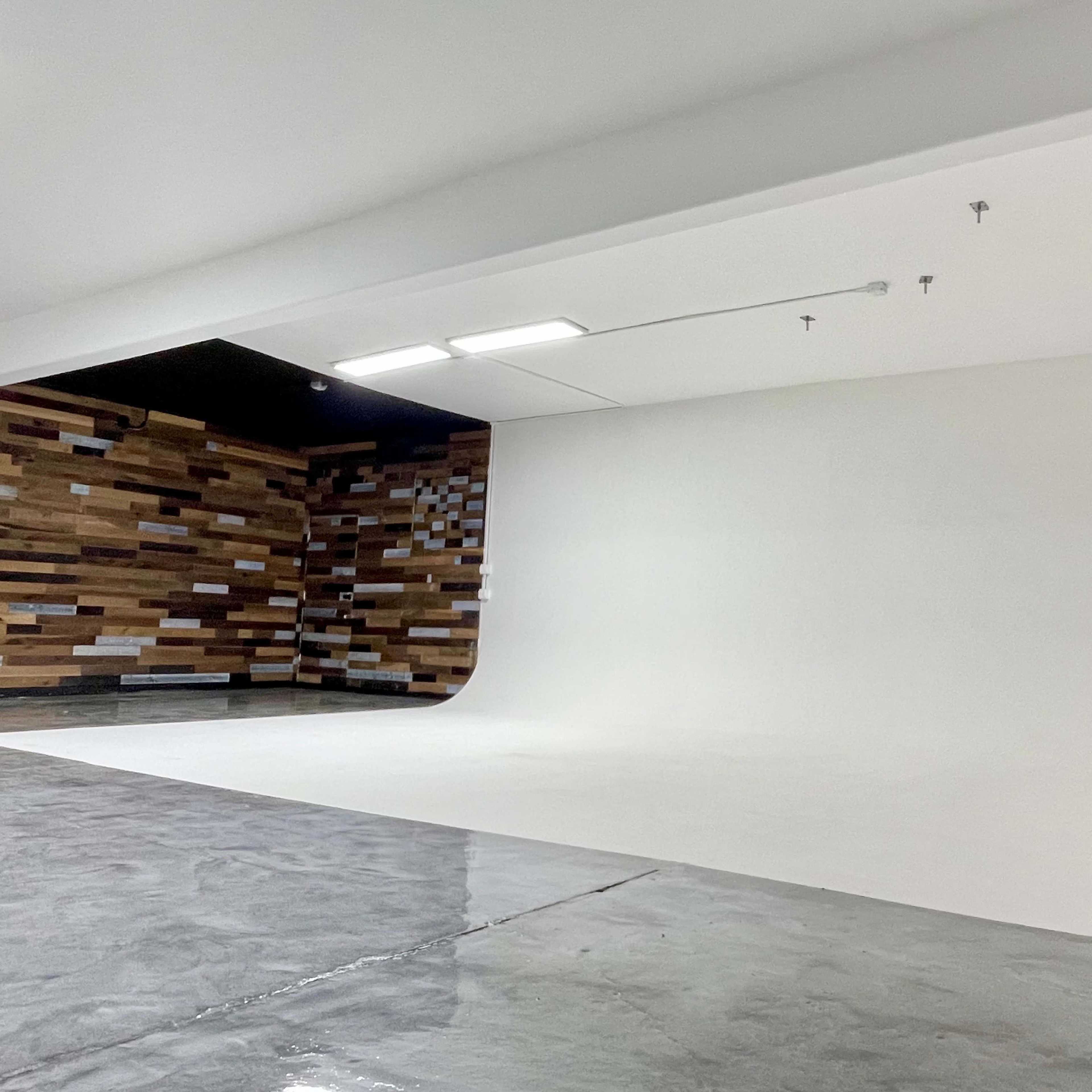 A spacious photography studio featuring a seamless white backdrop and a wooden accent wall.