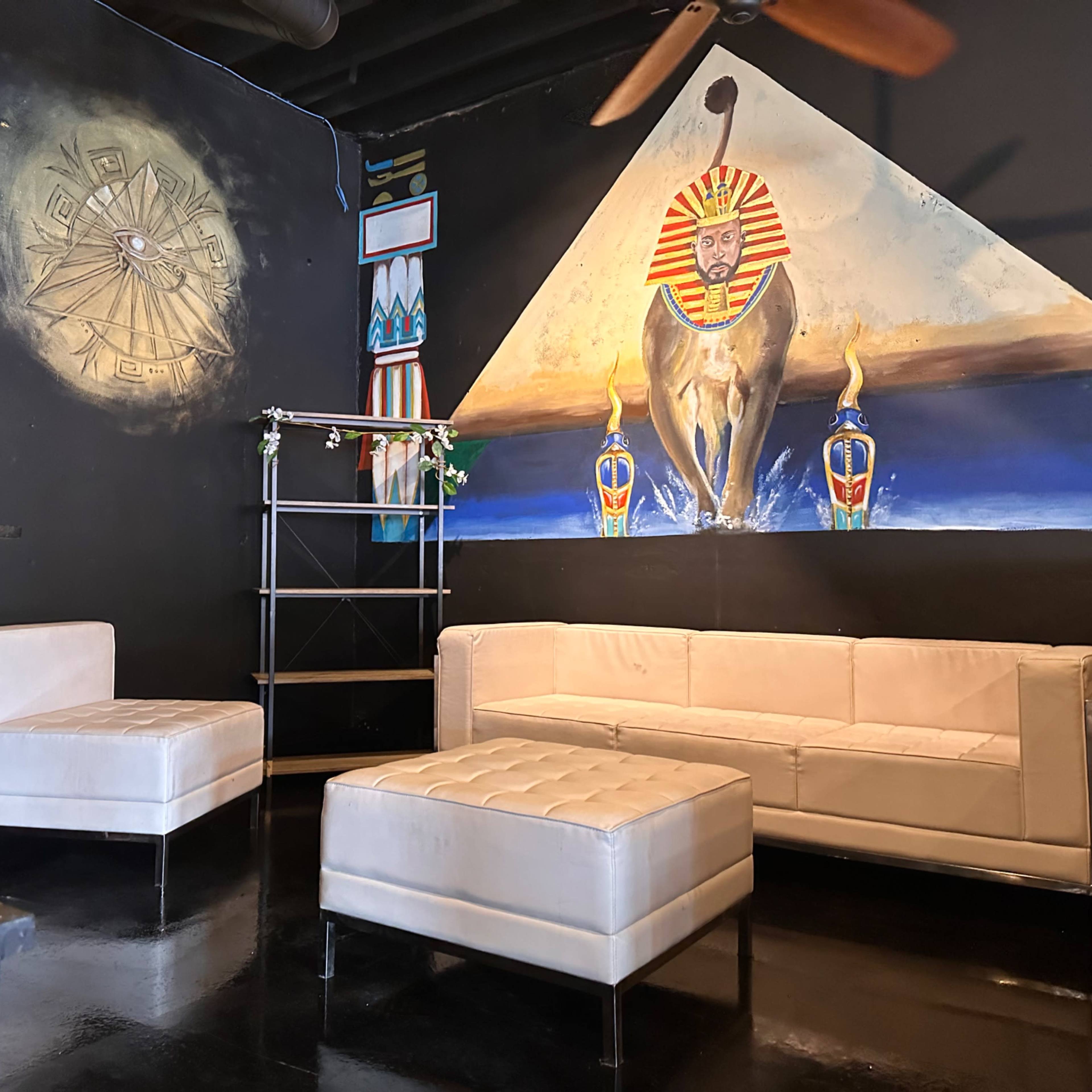 A lounge area with white furniture, featuring an artistic mural of a lion and Egyptian motifs on the wall.