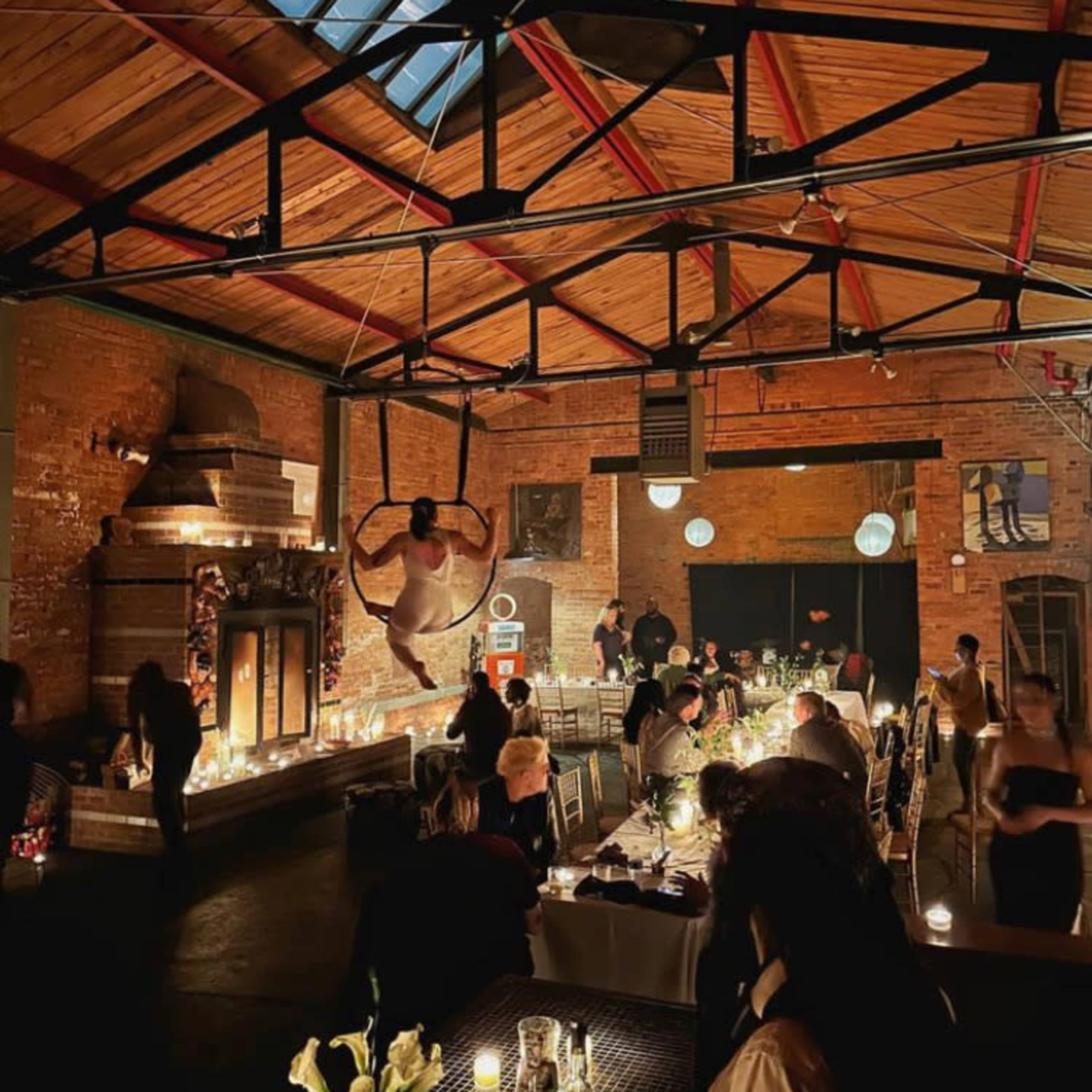 The scene depicts a dimly lit restaurant with a performer suspended from a hoop in the air, surrounded by diners at elegantly set tables.