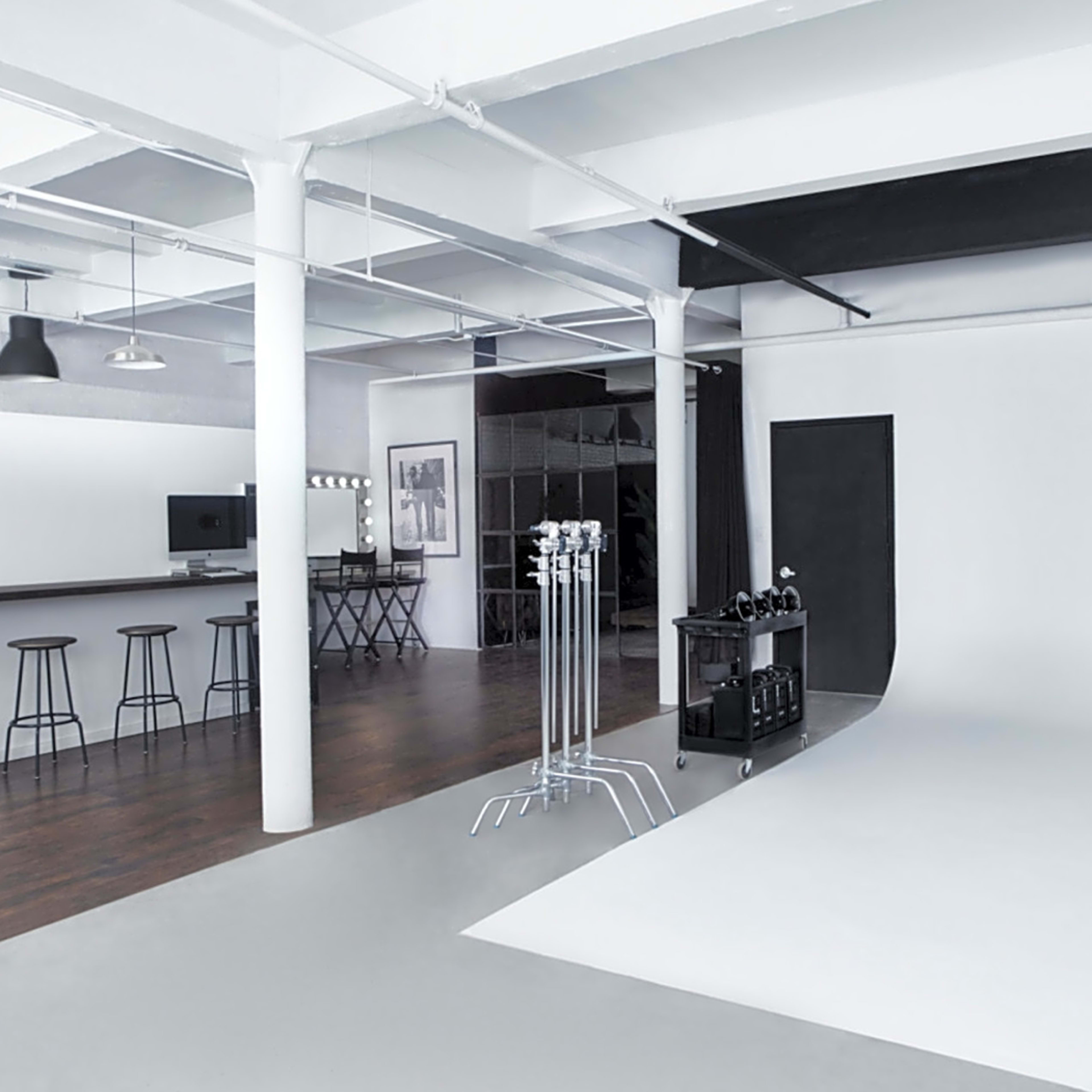 A spacious studio with a bar area, tall stools, and a plain white backdrop for photography.