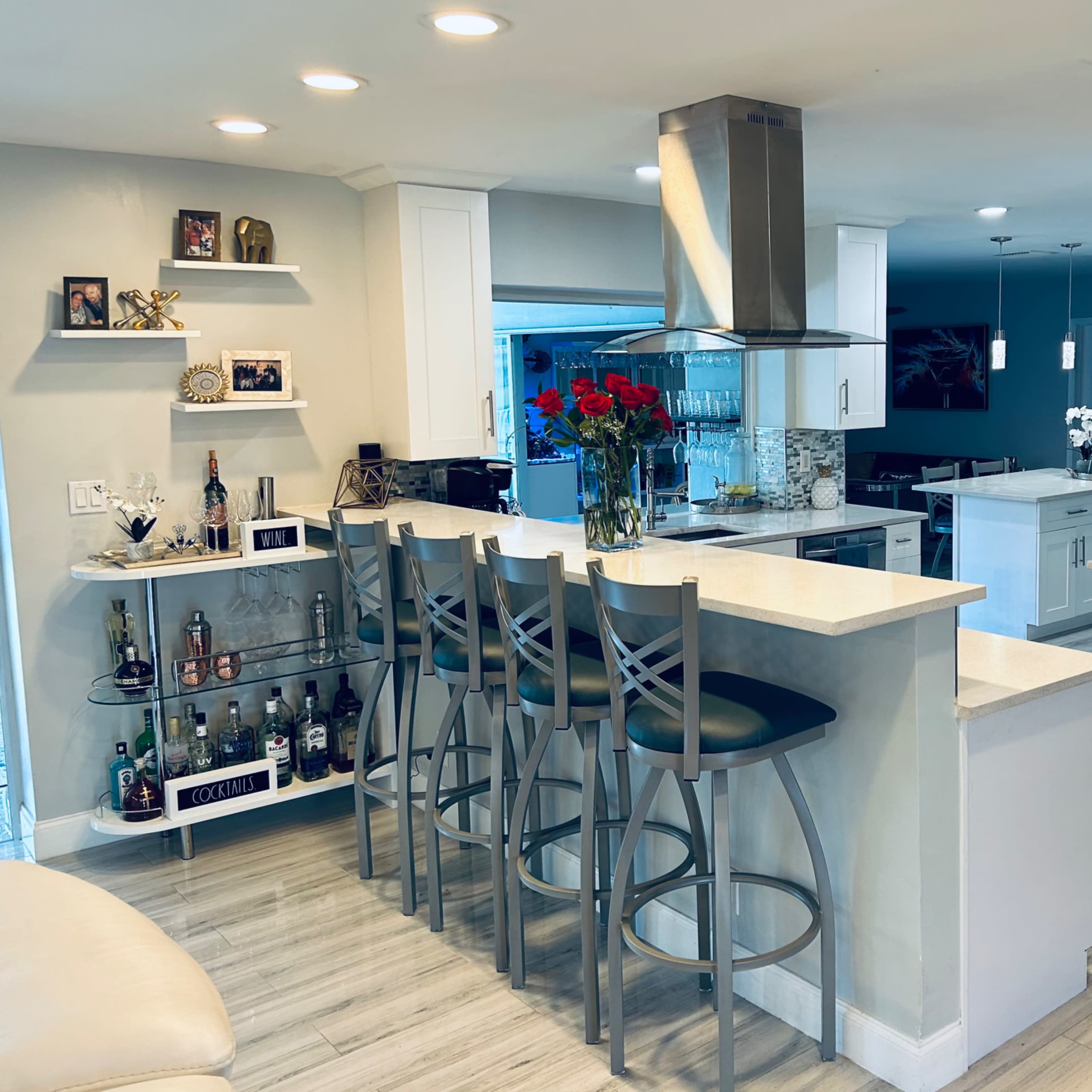 A modern kitchen with a central island featuring bar stools, stainless steel appliances, and glass cabinetry.